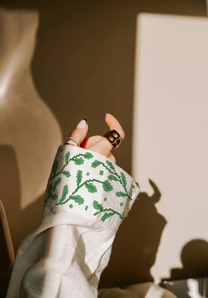 Hand wearing a white sleeve with green cross-stitch pattern, holding a phone.