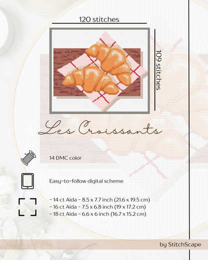 Cross-stitch pattern for croissants on a wooden surface with text and dimensions.