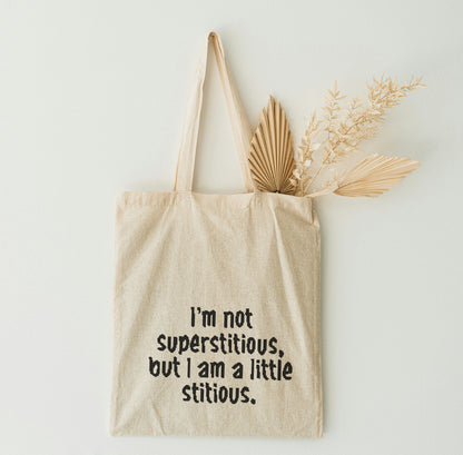 Beige tote bag with humorous text and dried plants on a light background