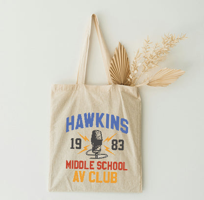 Beige tote bag with 'Hawkins 1983 Middle School Art Club' text and design on a light background.