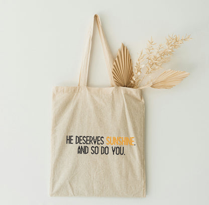A beige tote bag with a text hanging on the white wall