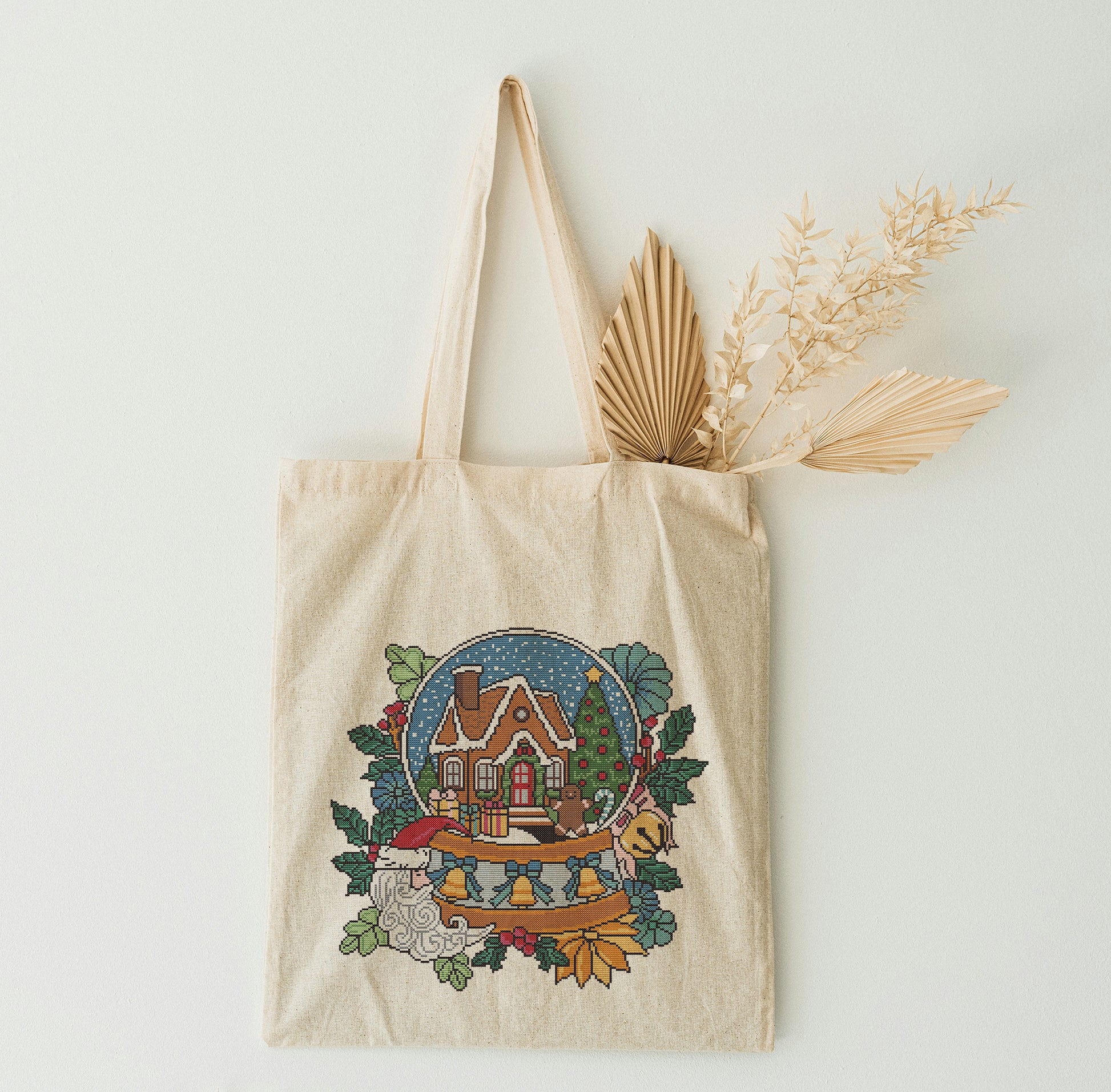 Beige tote bag with a festive design featuring a house and trees, on a light background.