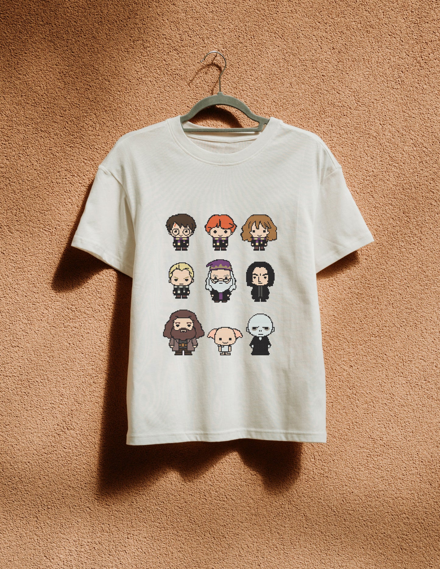 White t-shirt with character illustrations on a hanger against a brown textured wall