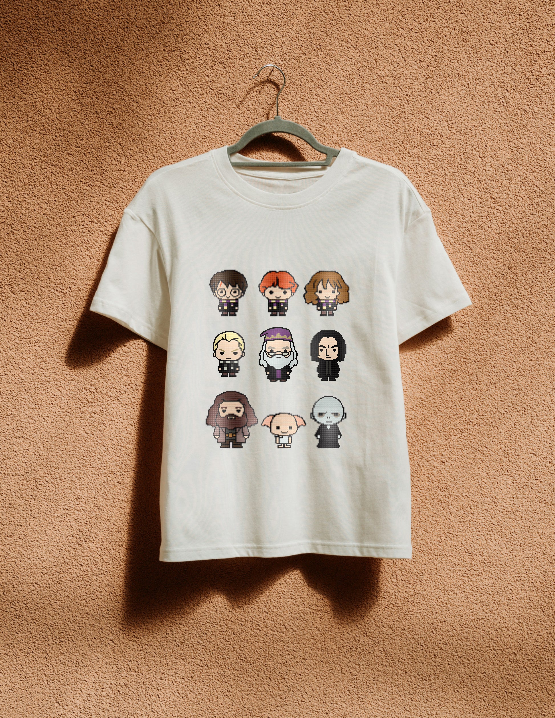 White t-shirt with character illustrations on a hanger against a brown textured wall