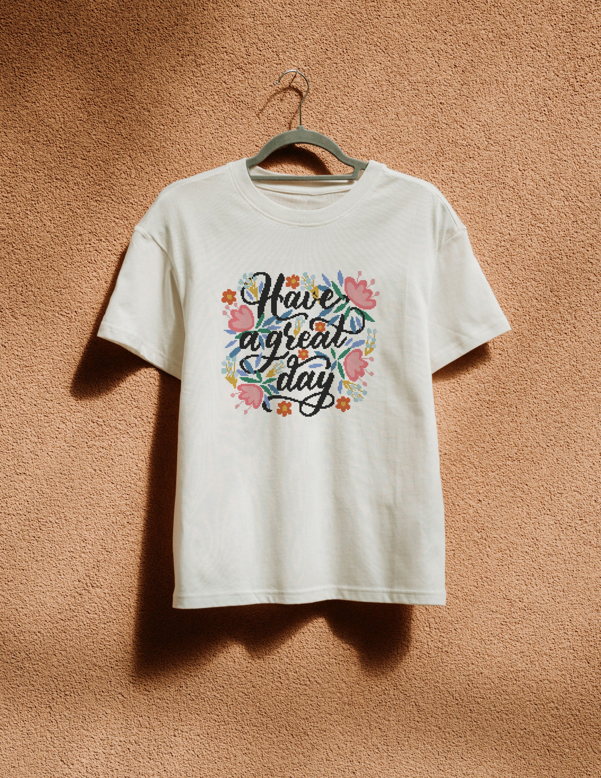 White t-shirt with colorful text and floral design on a hanger against a brown background