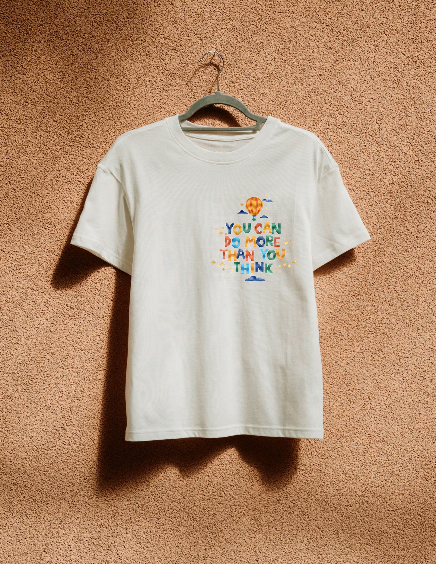 White t-shirt with colorful text and graphics on a beige wall