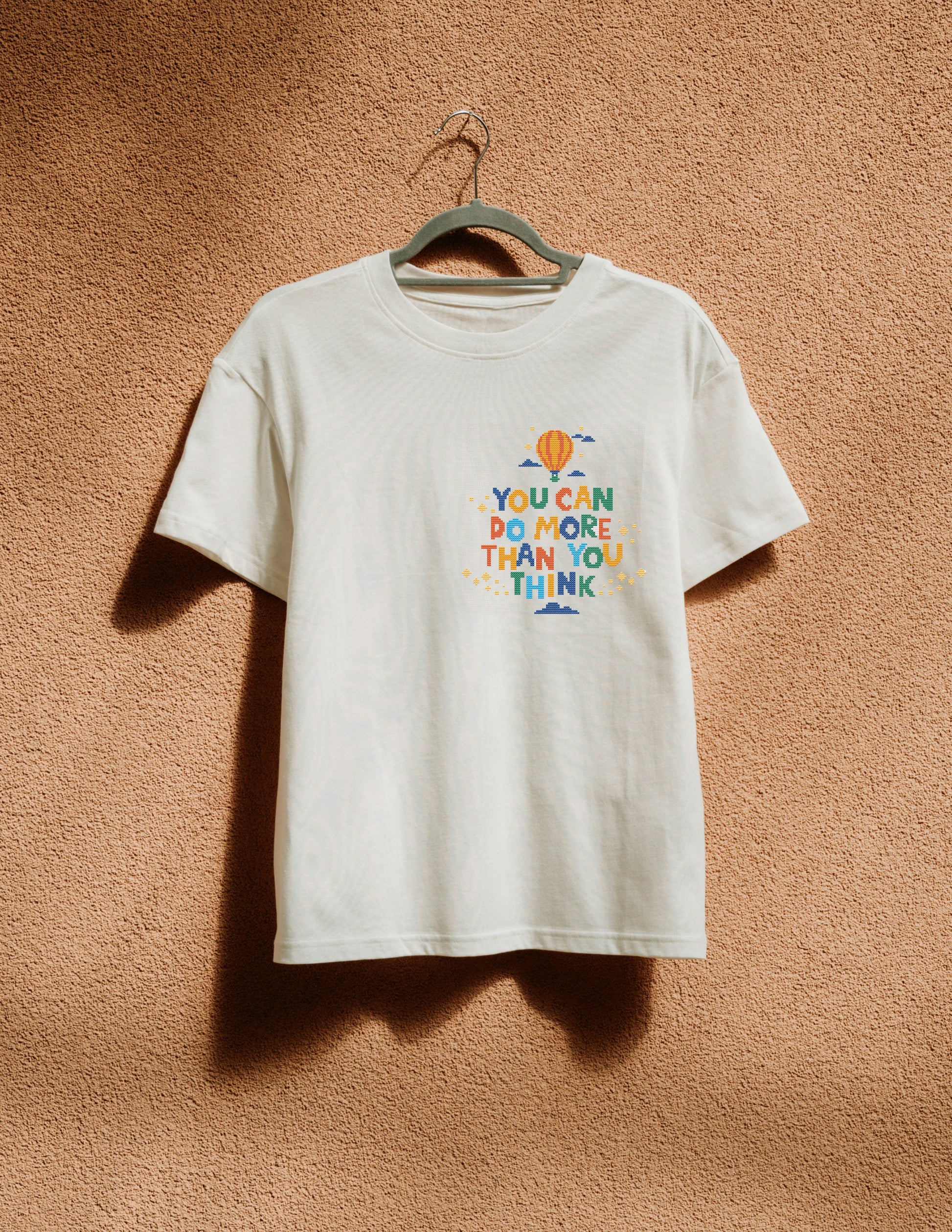 White t-shirt with colorful text and graphics on a beige wall