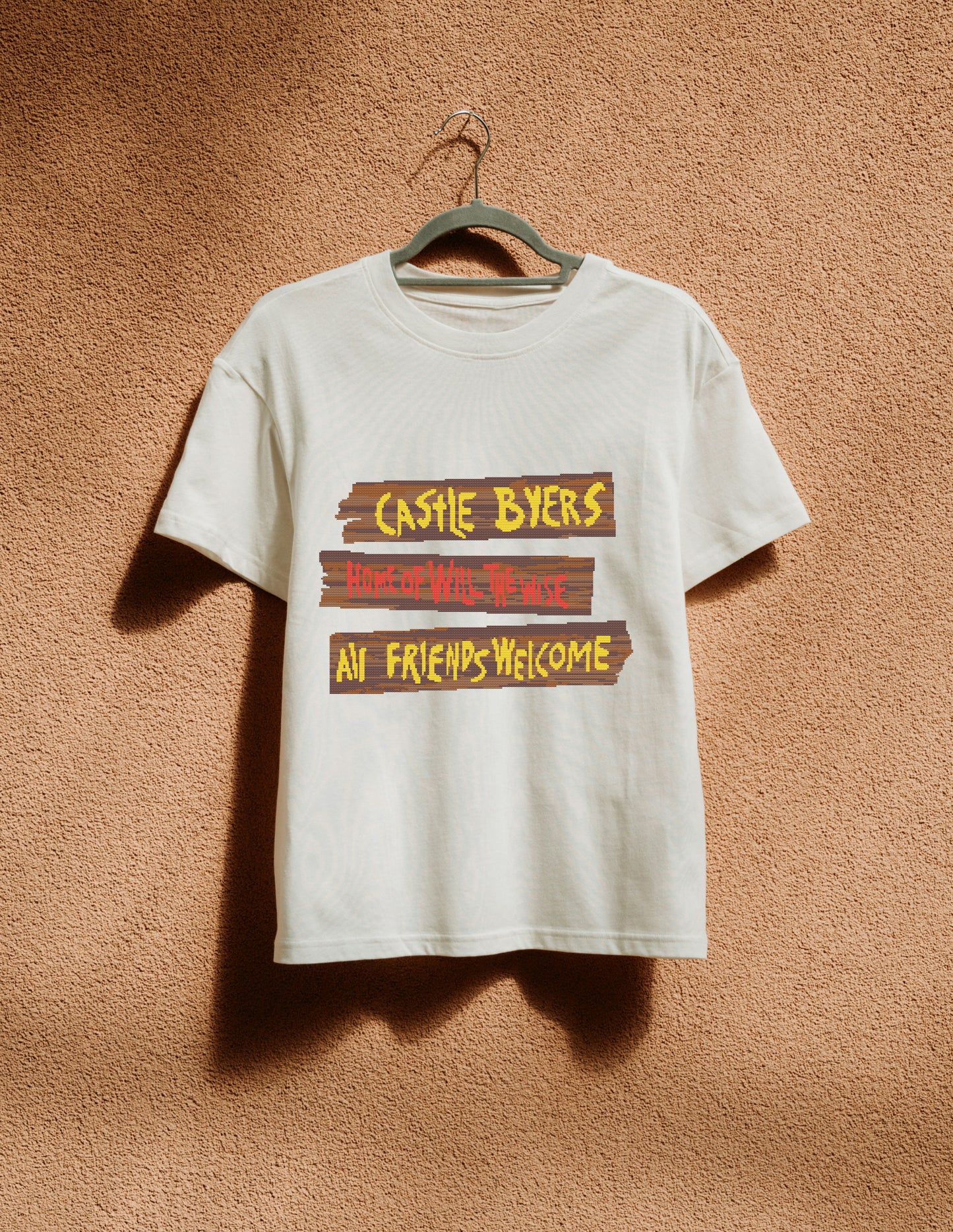White t-shirt with text design on a hanger against a textured brown wall