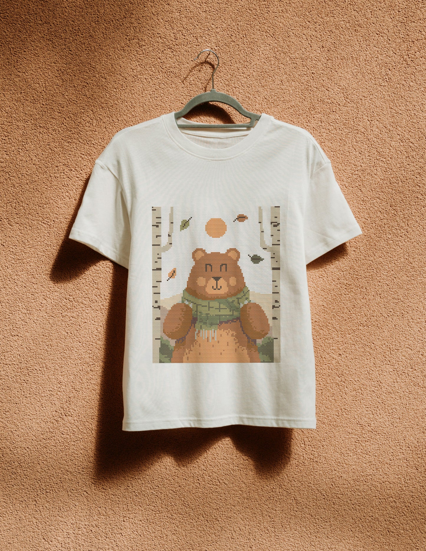 White t-shirt with a bear graphic on a hanger against a brown textured wall