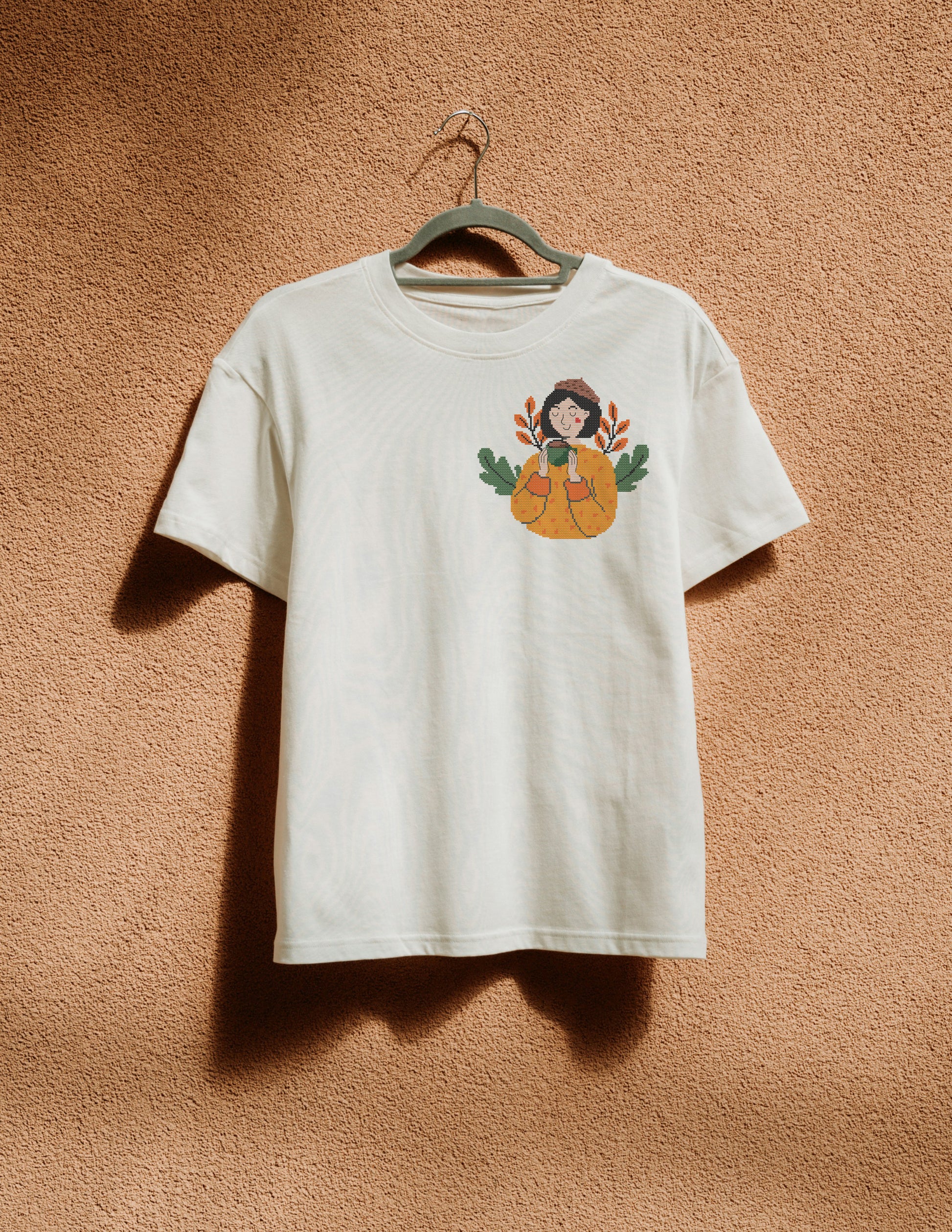 White t-shirt with a graphic design of a person with pumpkins on a beige wall.