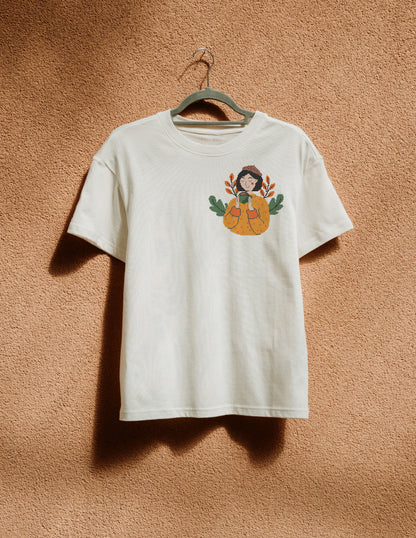 White t-shirt with a graphic design of a person with pumpkins on a beige wall.