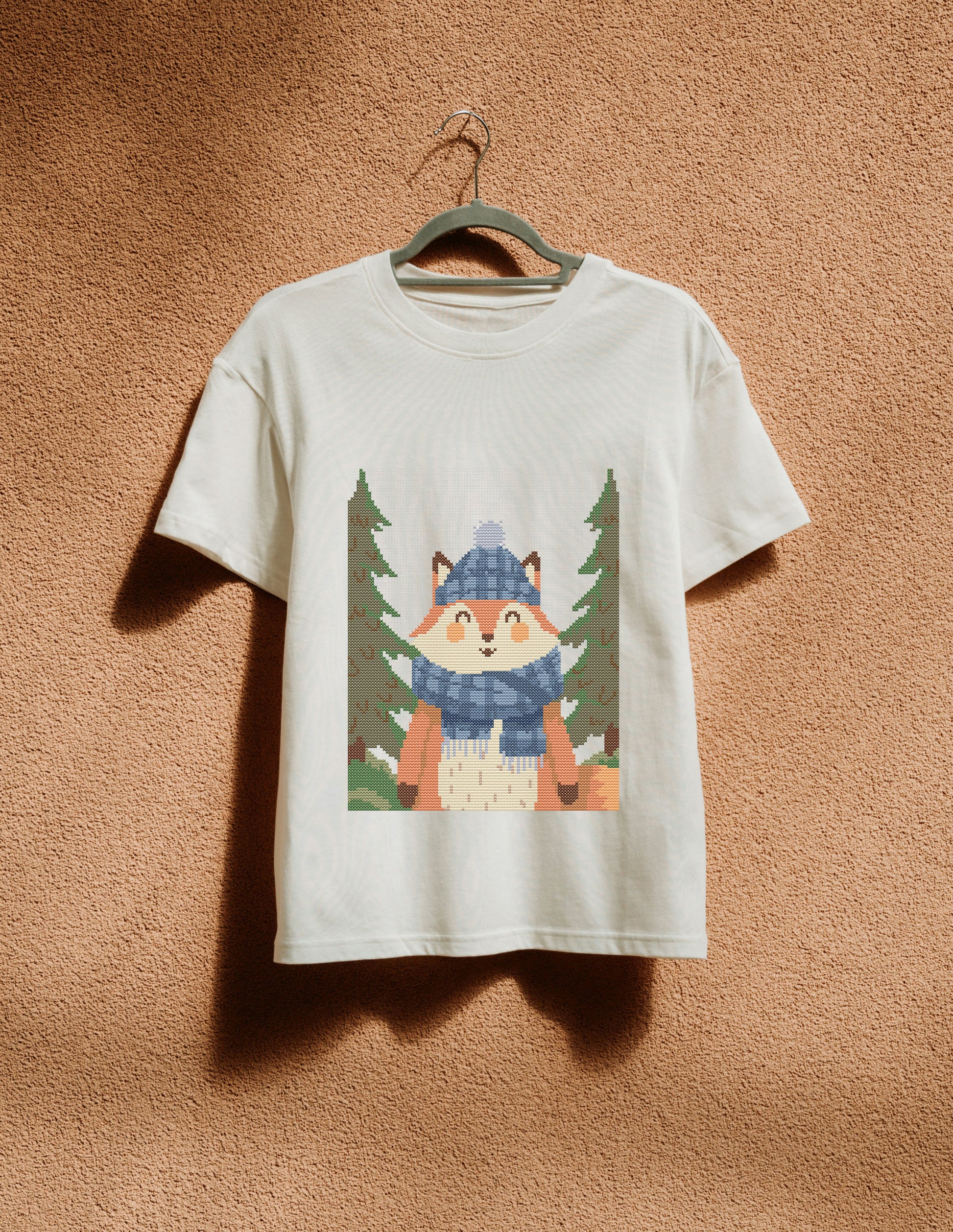 White t-shirt with a fox graphic hanging on a hanger against a brown textured wall.