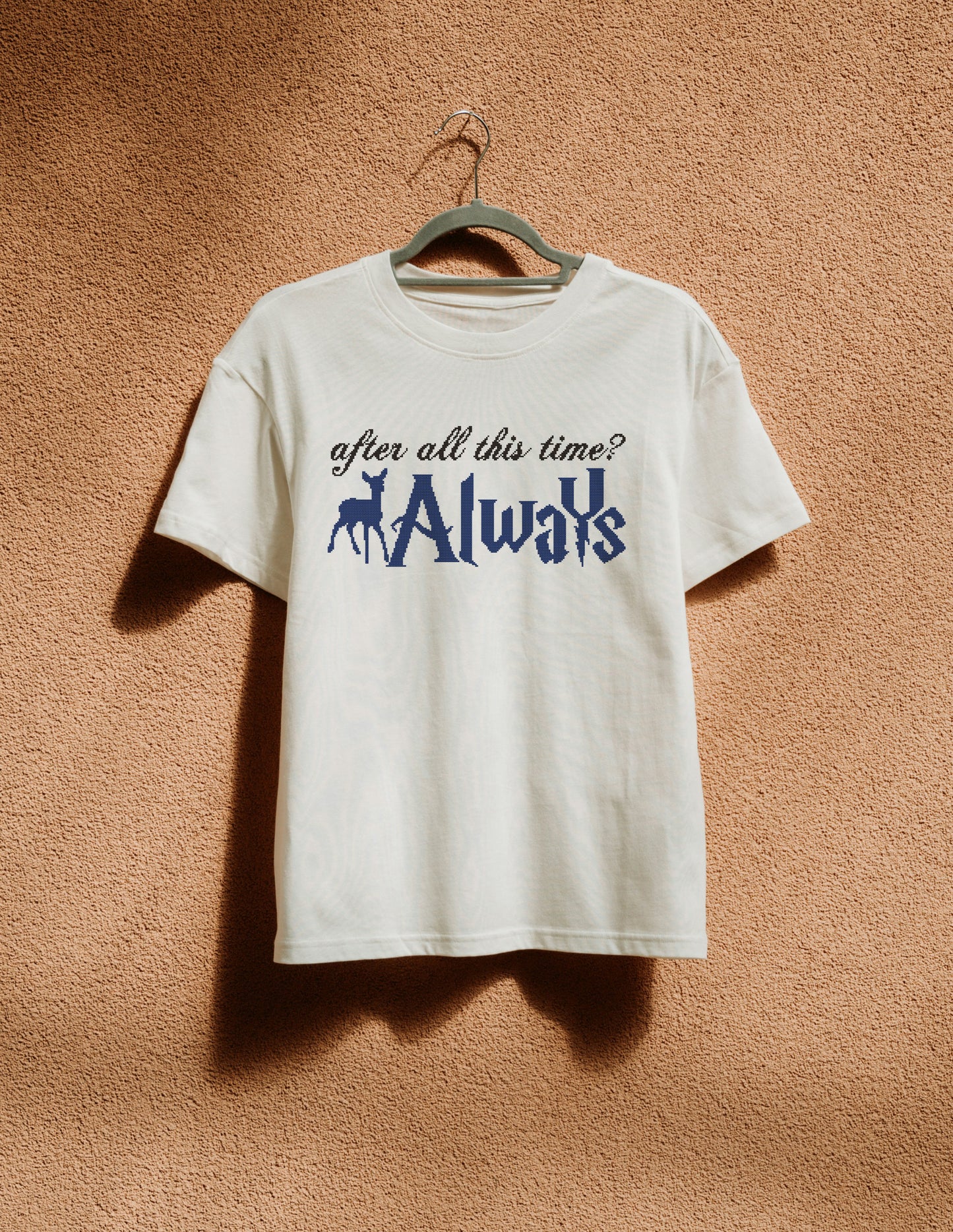 White t-shirt with text and graphic on a hanger against a brown textured wall