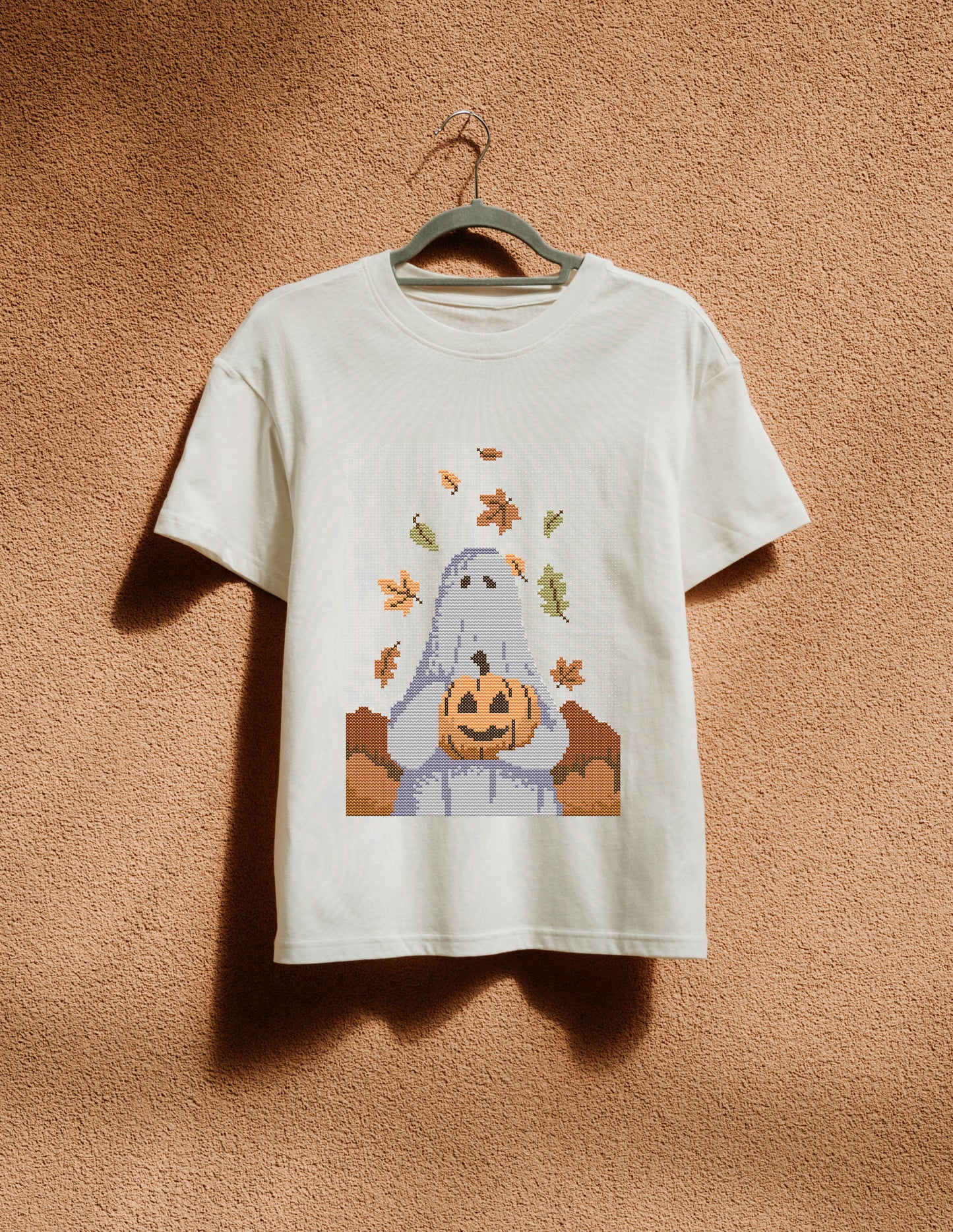 White t-shirt with a ghost holding a pumpkin design on a beige background