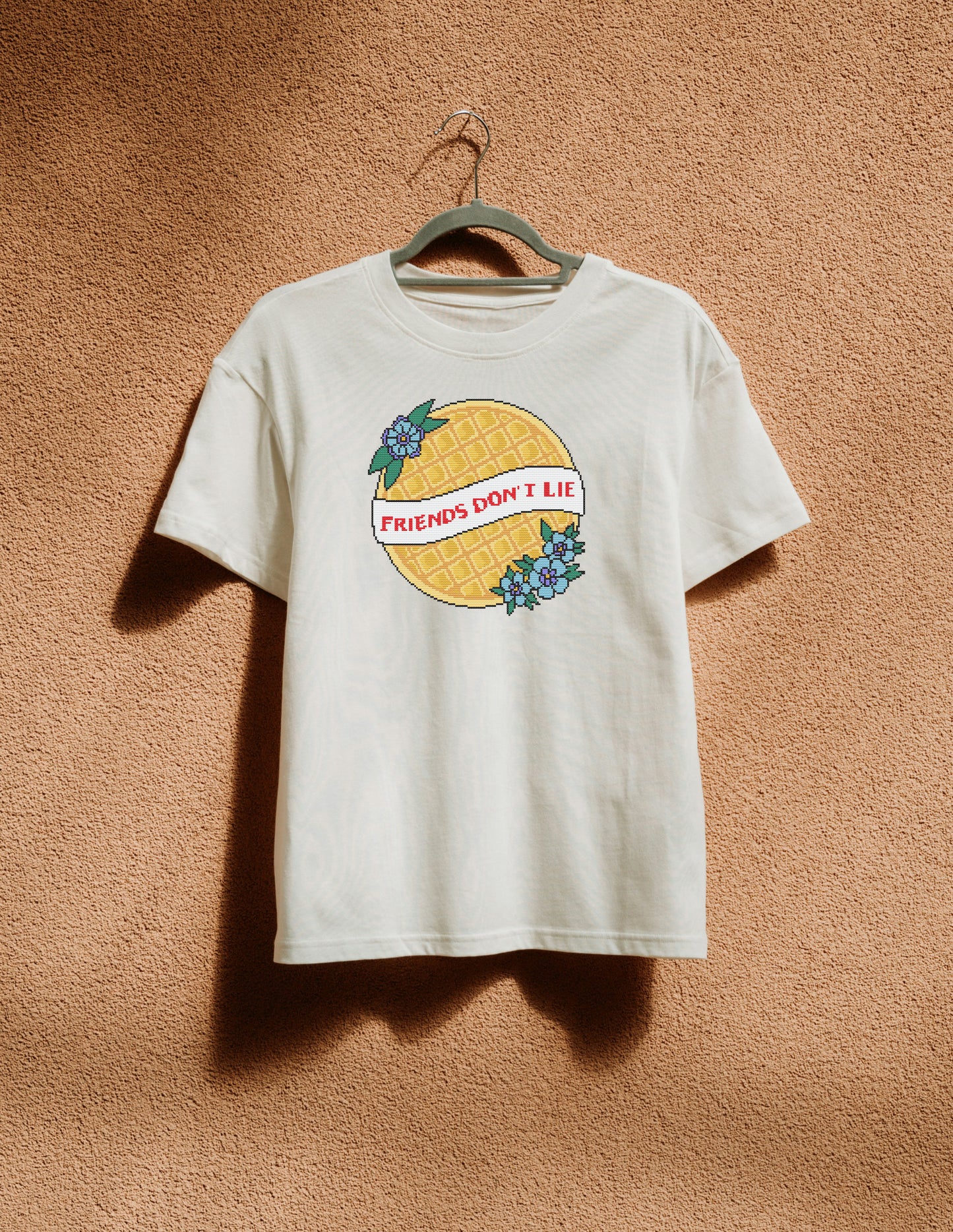 White t-shirt with graphic design hanging on a hanger against a brown textured wall