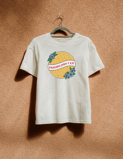 White t-shirt with graphic design hanging on a hanger against a brown textured wall