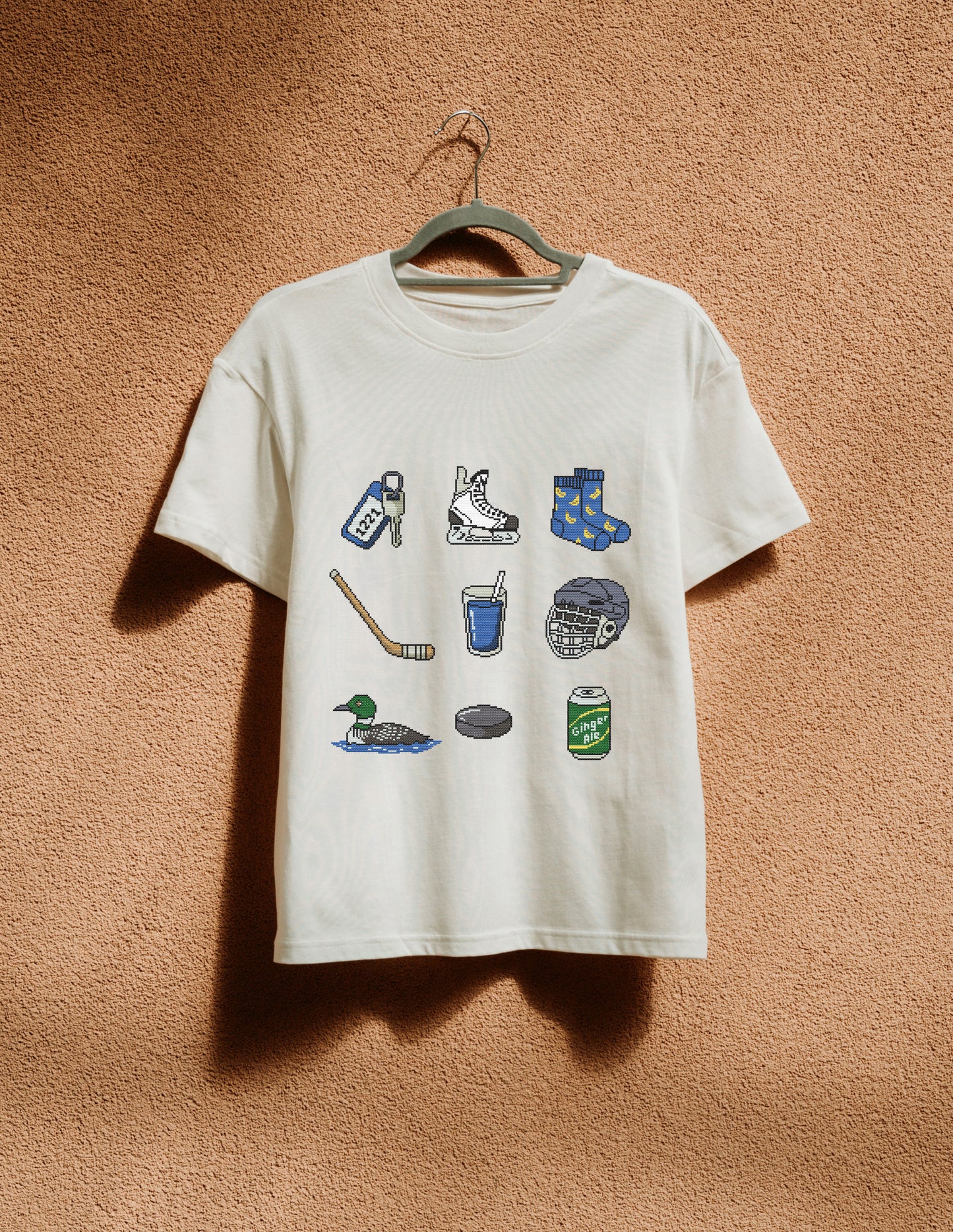 White t-shirt with graphic designs on a hanger against a brown textured wall