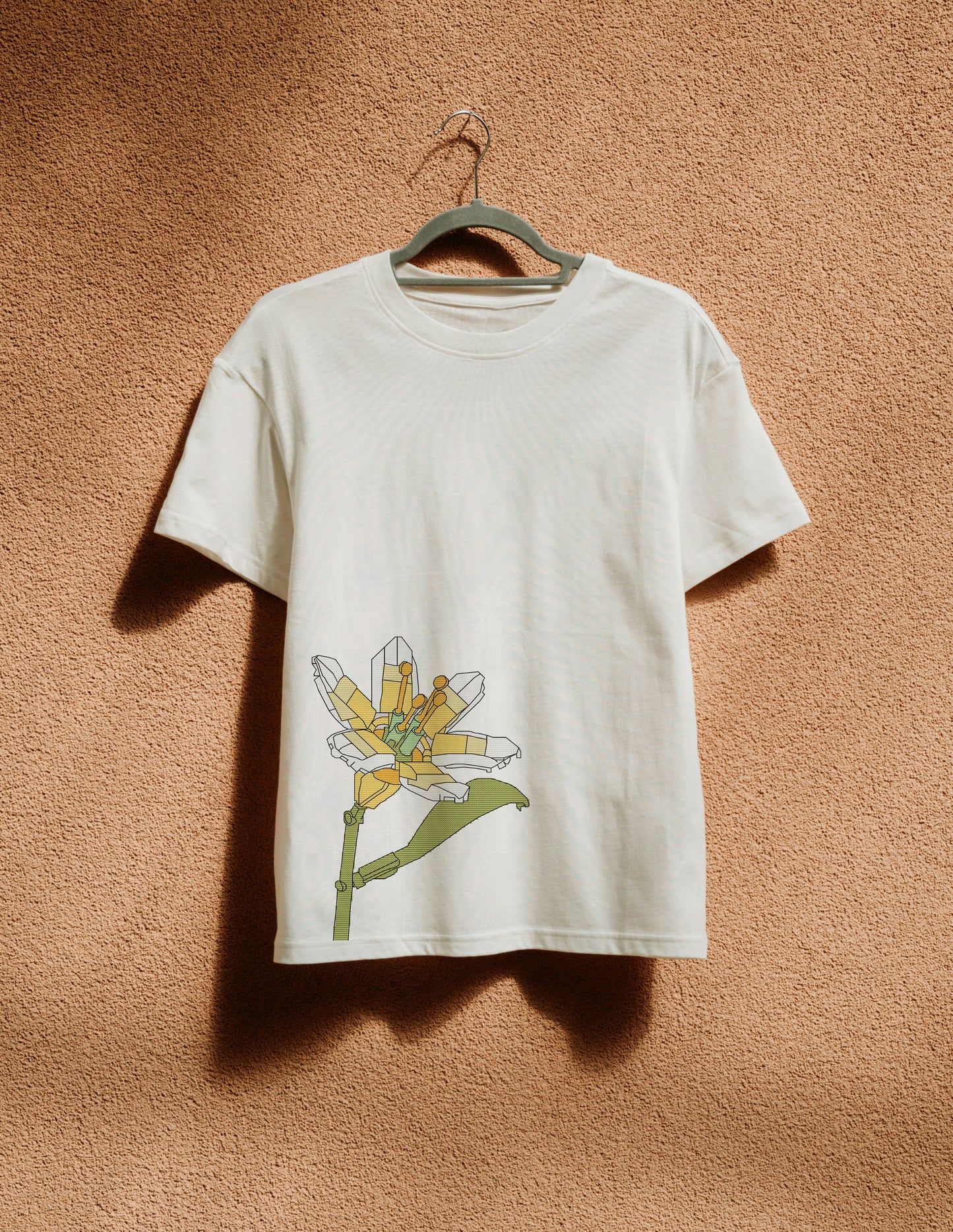 White t-shirt with a colorful flower design on a hanger against a brown textured wall.