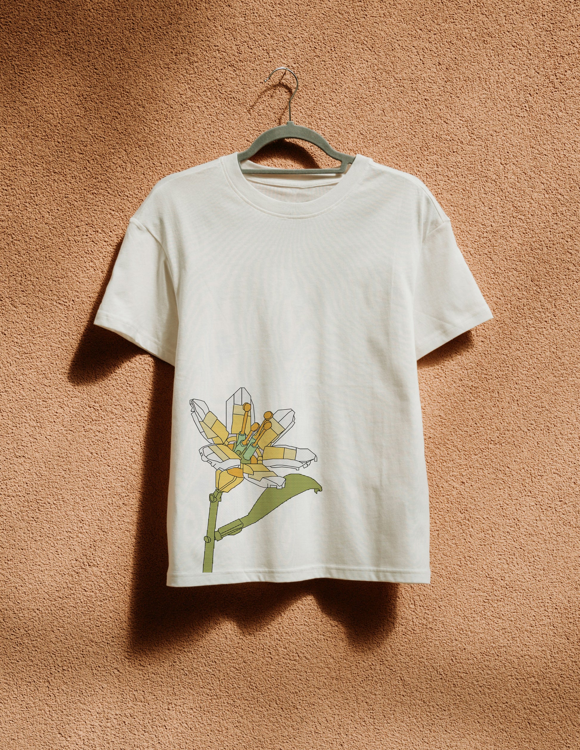White t-shirt with a colorful flower design on a hanger against a brown textured wall.