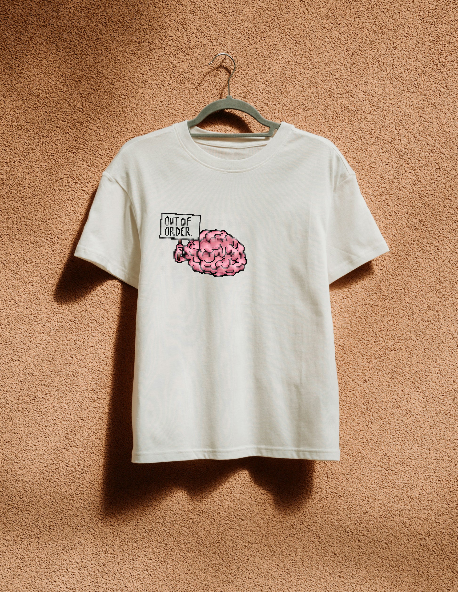White t-shirt with a pink brain graphic and text on a beige wall