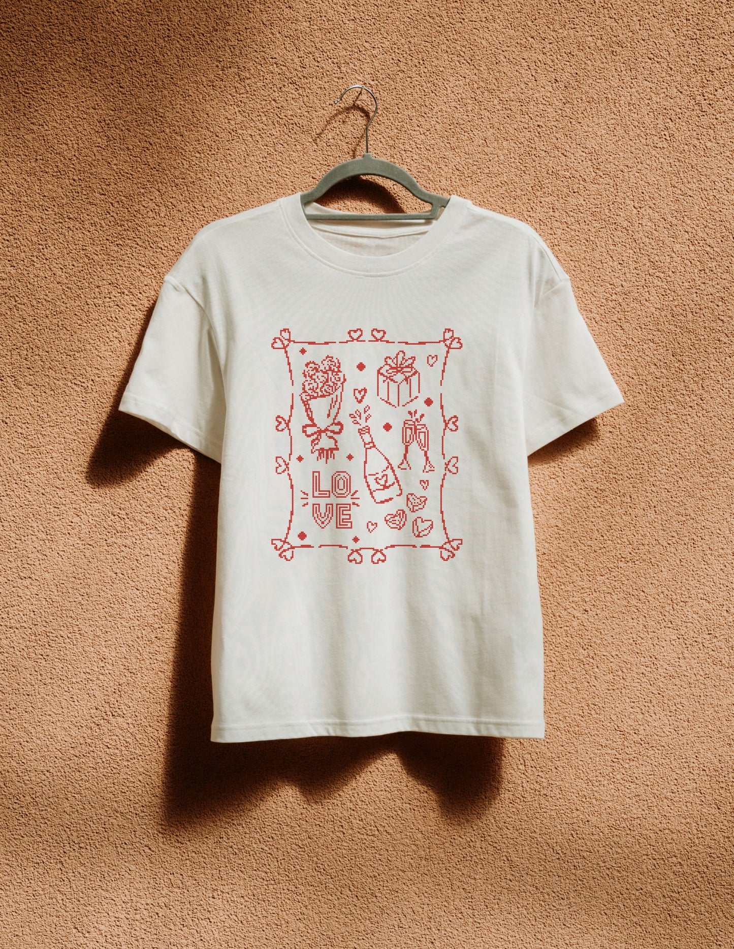 White t-shirt with red graphic design on a hanger against a brown textured wall