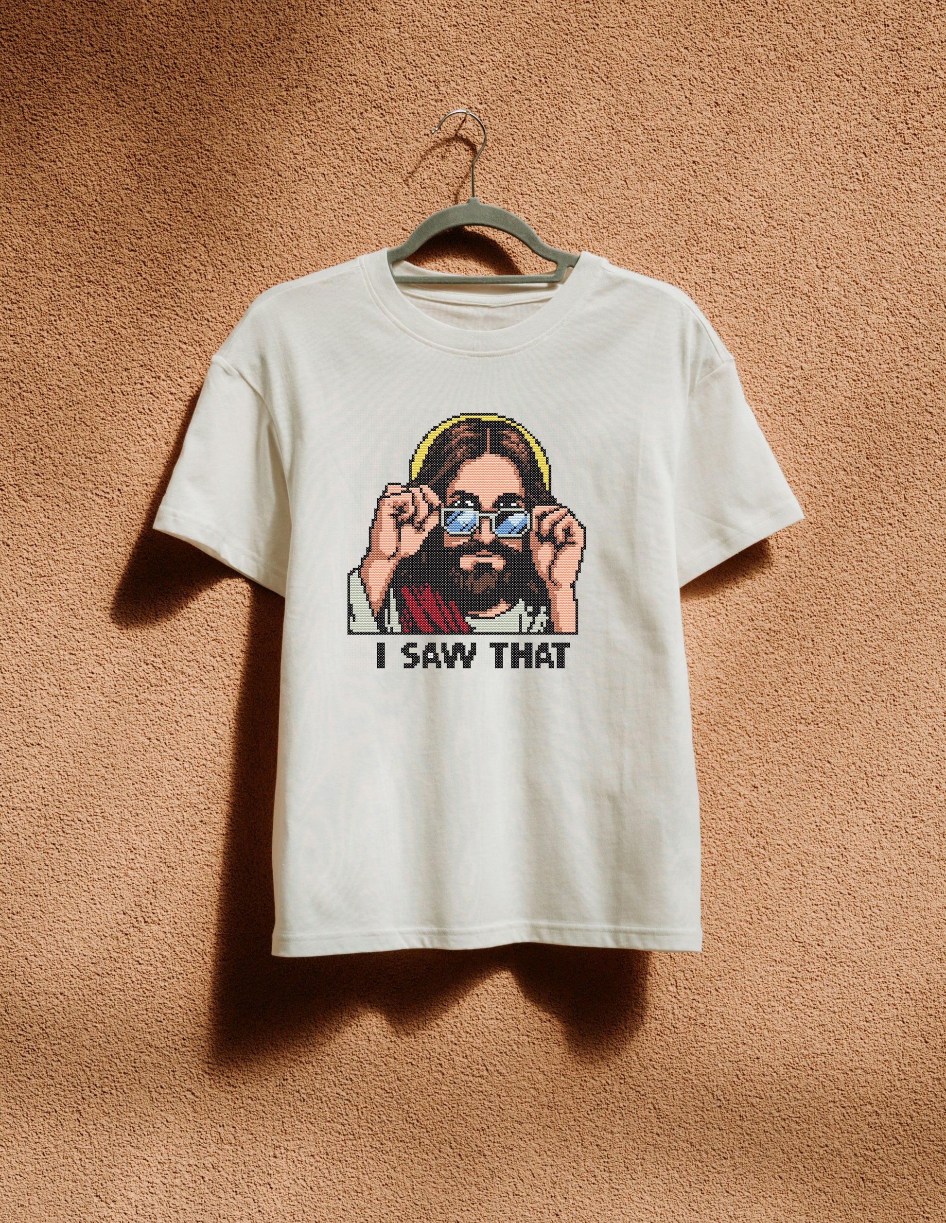 White t-shirt with graphic design of a person wearing sunglasses and text 'I SAW THAT' on a beige background.