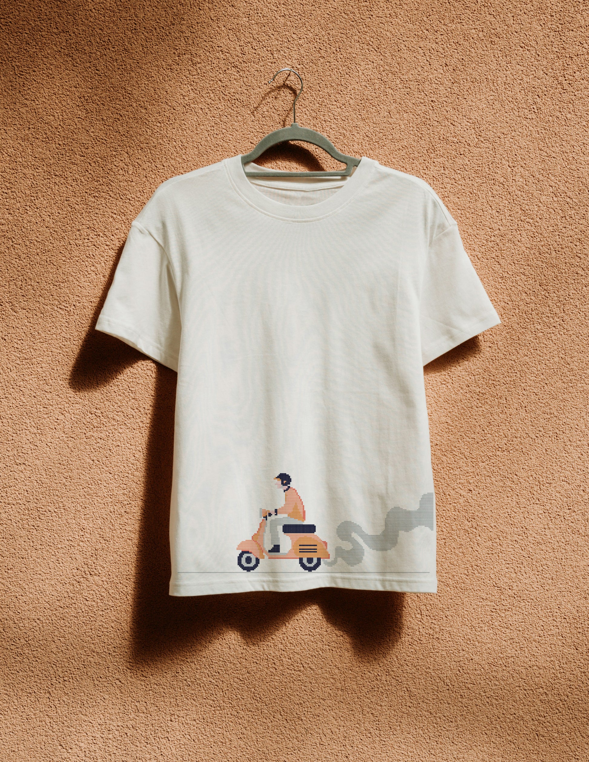 White t-shirt with graphic design on a hanger against a beige wall