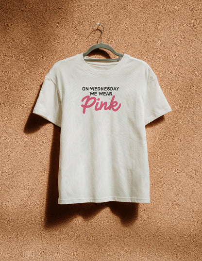 White t-shirt with 'BITCHIN'' in red on a hanger against a brown textured wall.