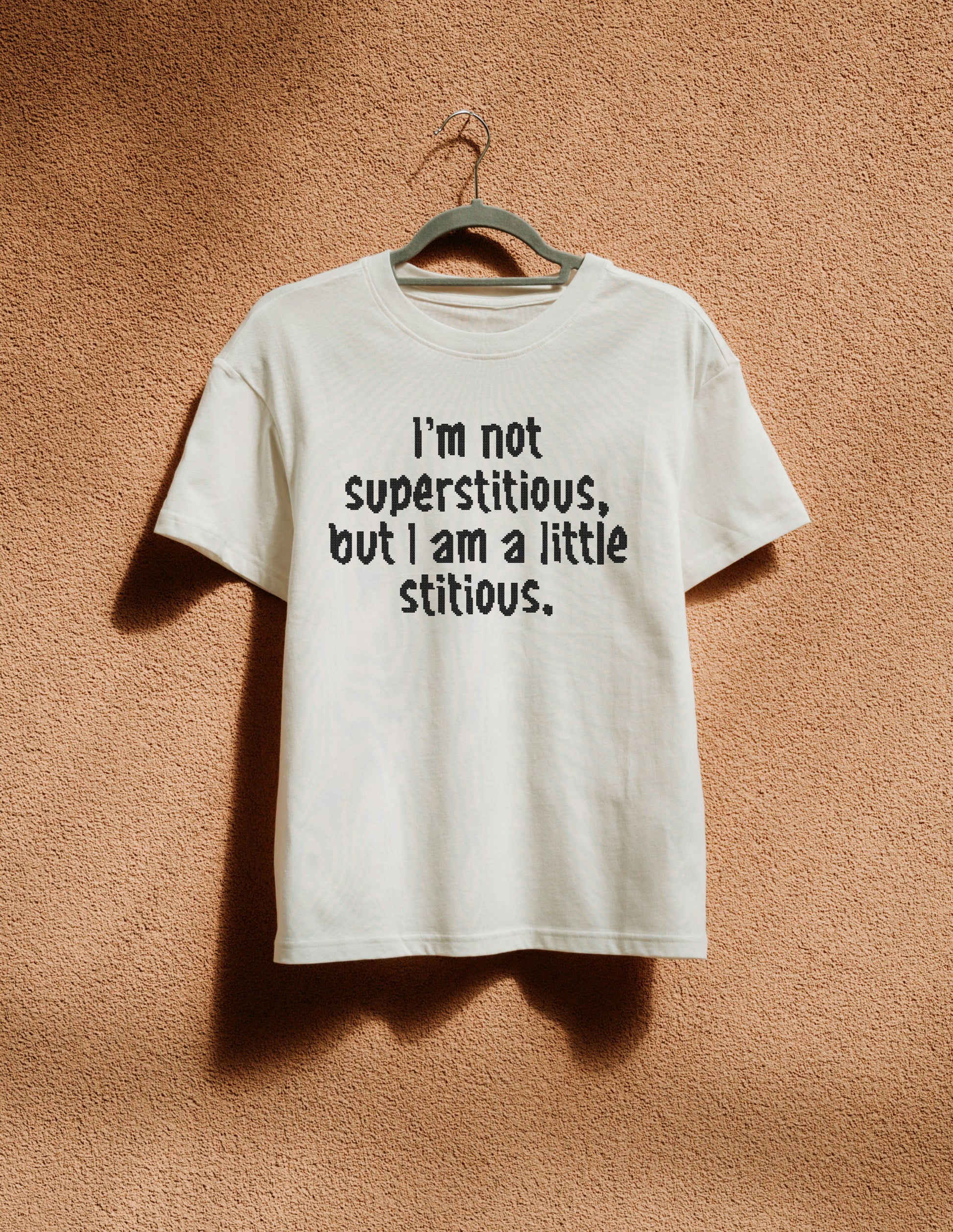 White t-shirt with humorous text on a hanger against a textured brown wall
