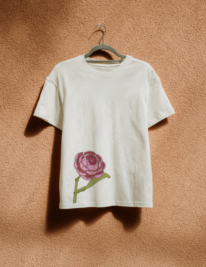 White t-shirt with a pink flower design on a hanger against a brown wall.