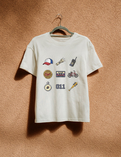 White t-shirt with various graphic designs on a hanger against a brown textured wall.
