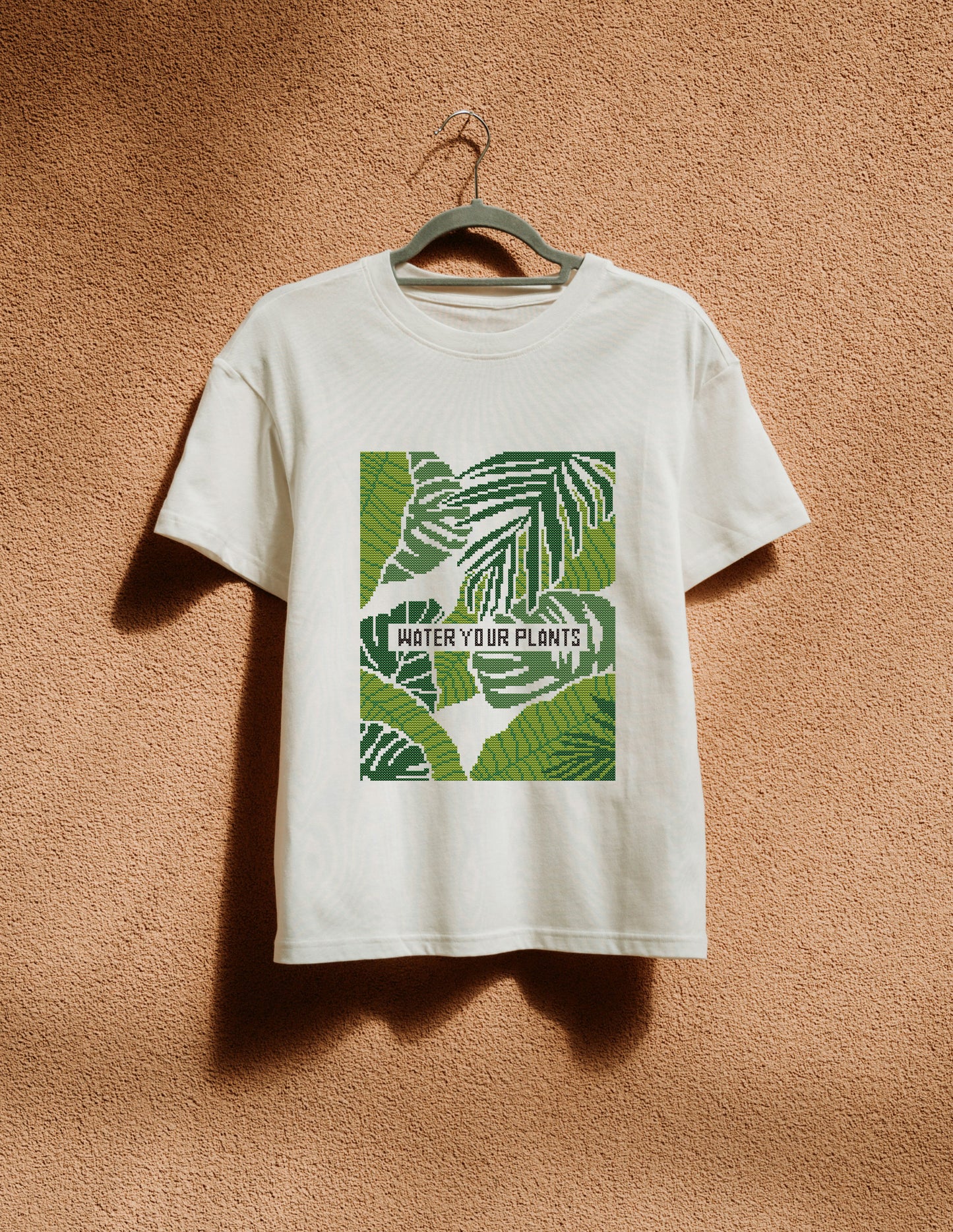 White t-shirt with green leaf design and text 'Water Your Plants' on a beige background