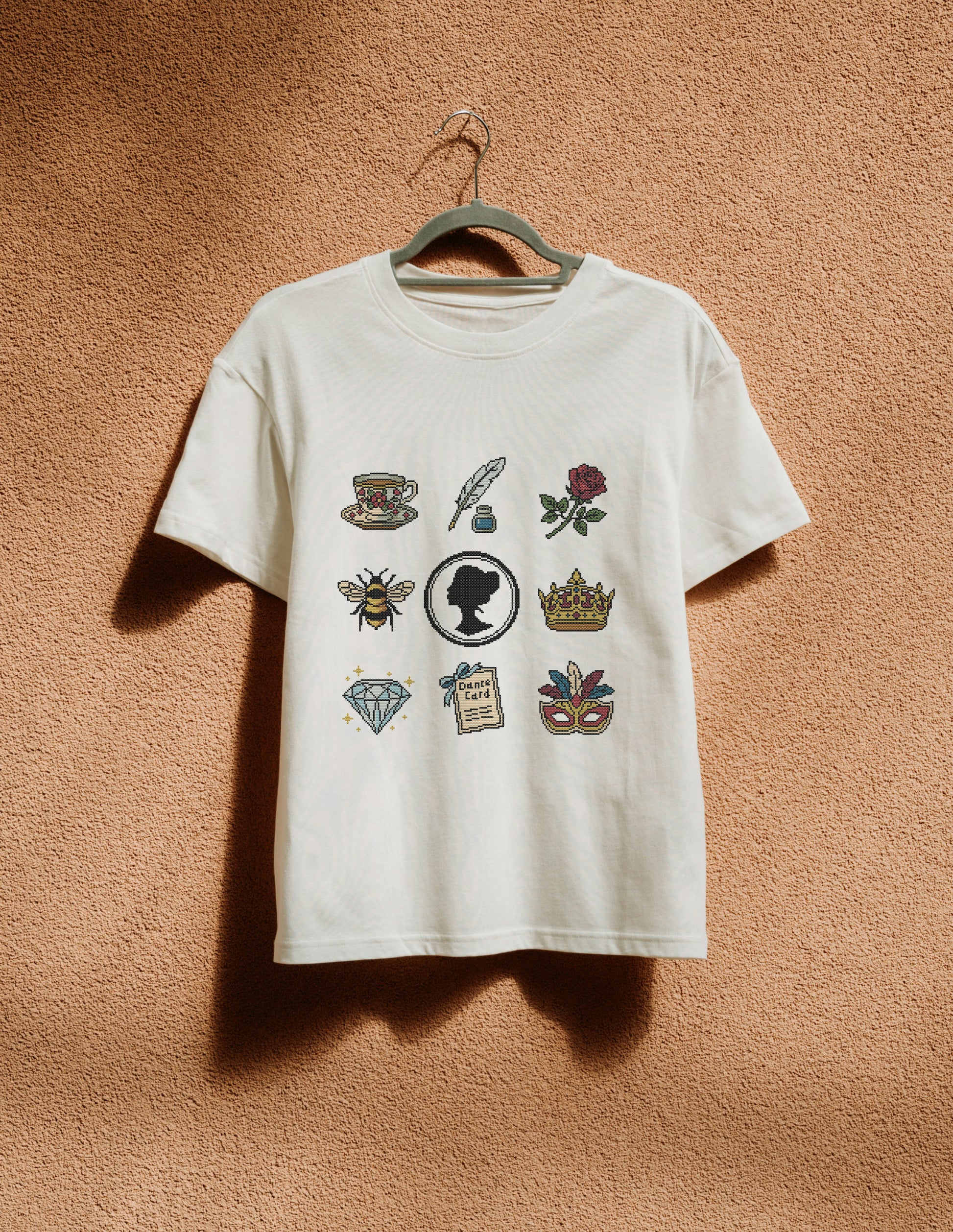 White t-shirt with various graphics on a hanger against a textured brown wall