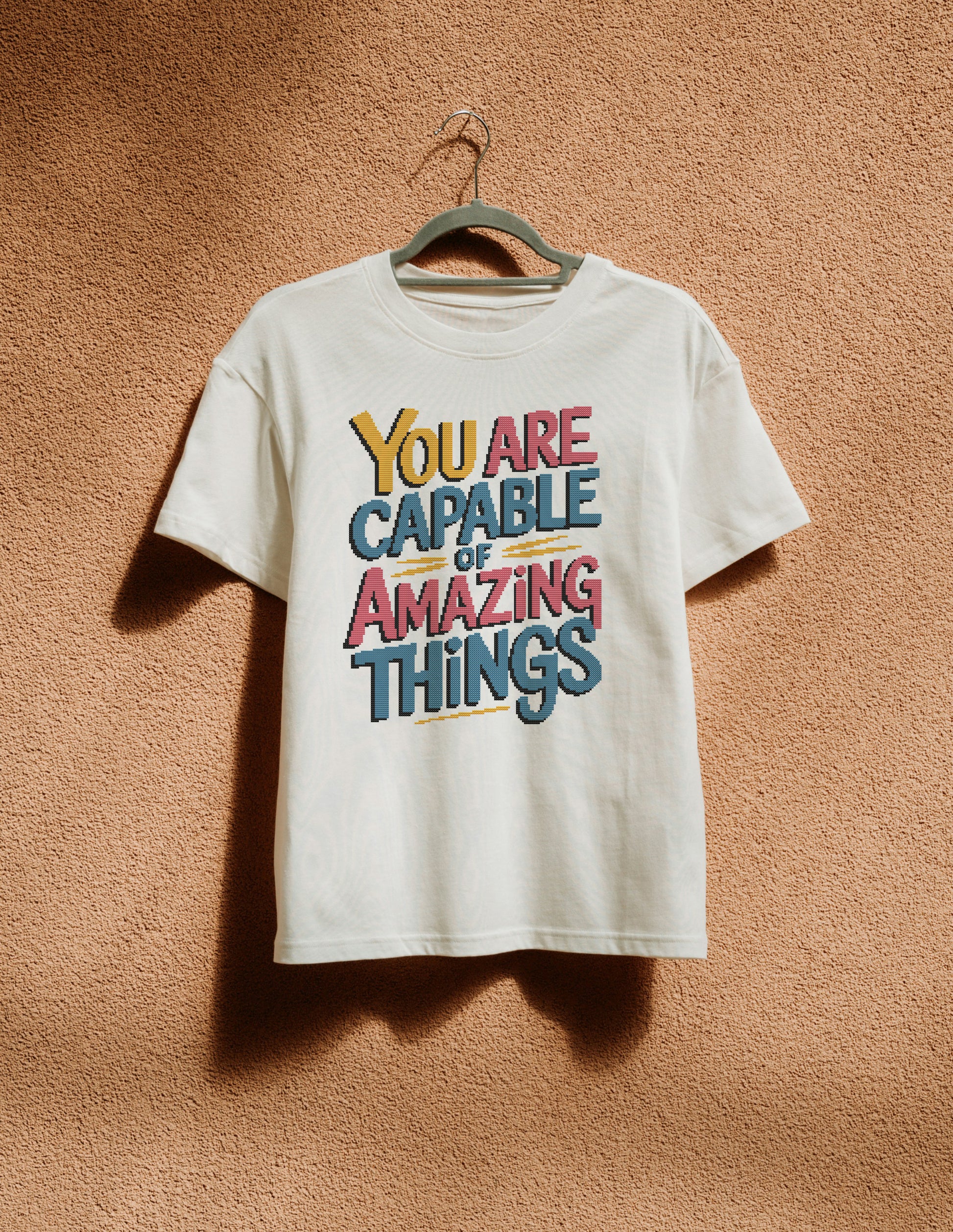 White t-shirt with motivational quote on a hanger against a textured brown wall