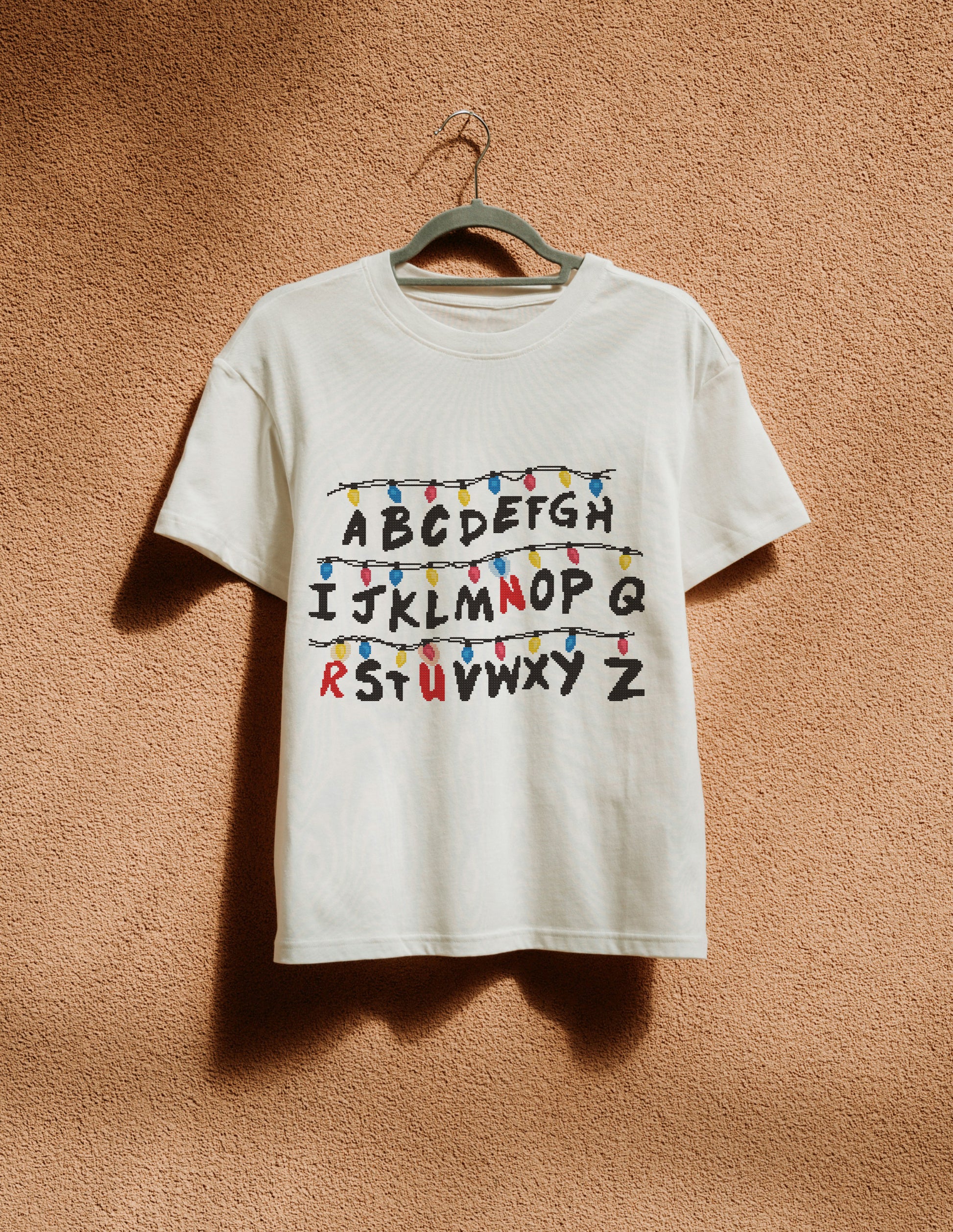 White t-shirt with colorful lettering on a hanger against a beige wall