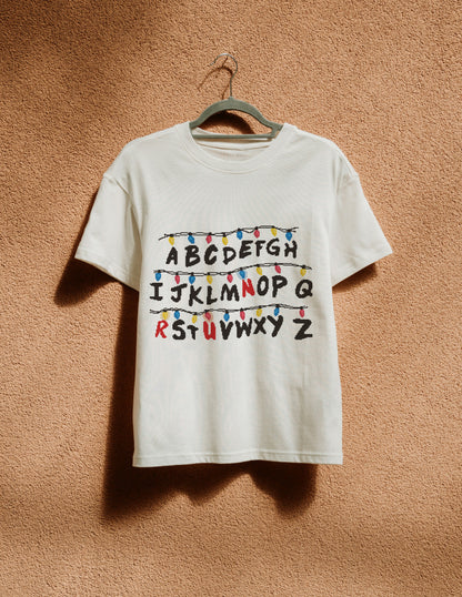 White t-shirt with colorful lettering on a hanger against a beige wall
