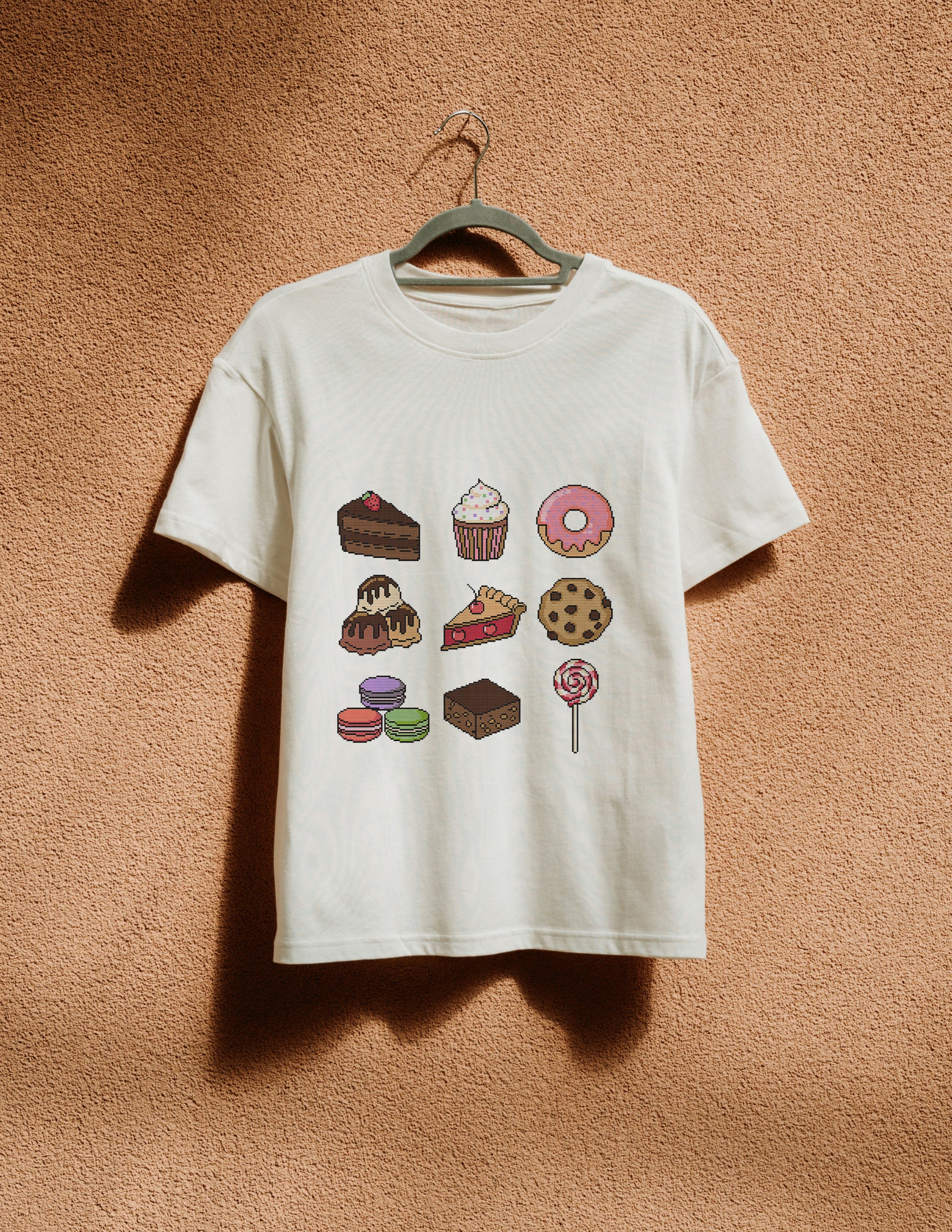 White t-shirt with dessert graphics on a hanger against a textured brown wall