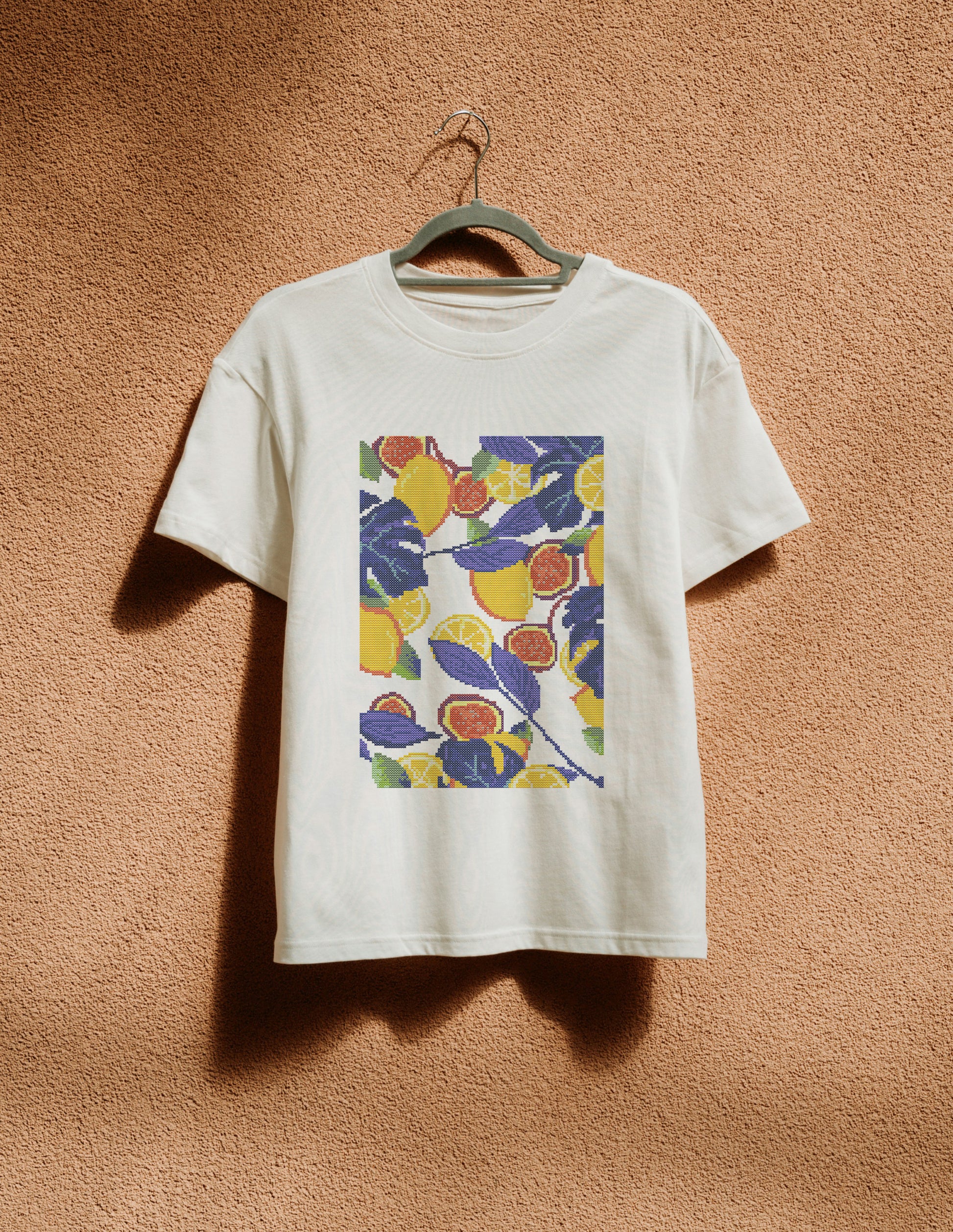 White t-shirt with colorful fruit pattern on a hanger against a brown textured wall