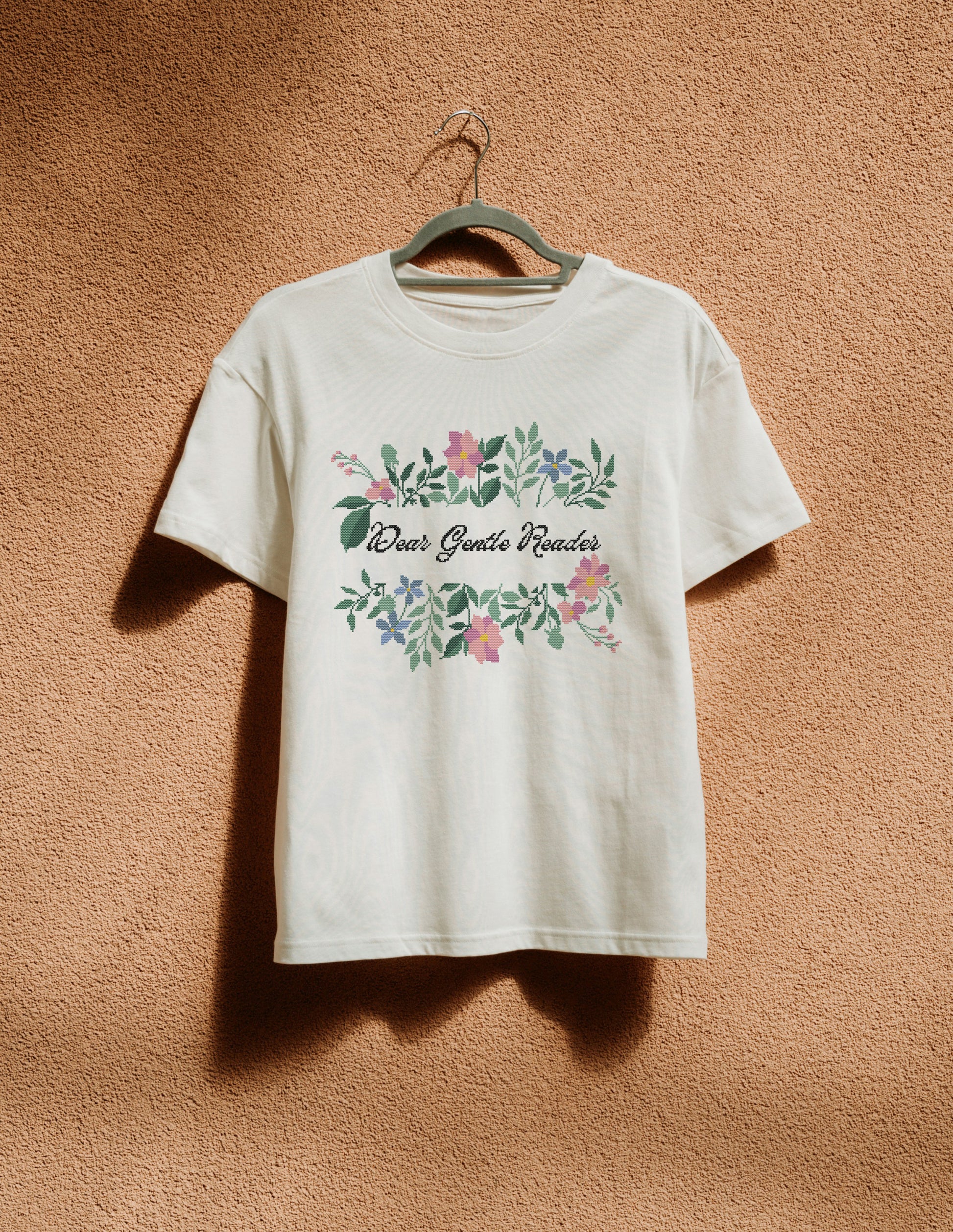 White t-shirt with floral design and text on a hanger against a brown background
