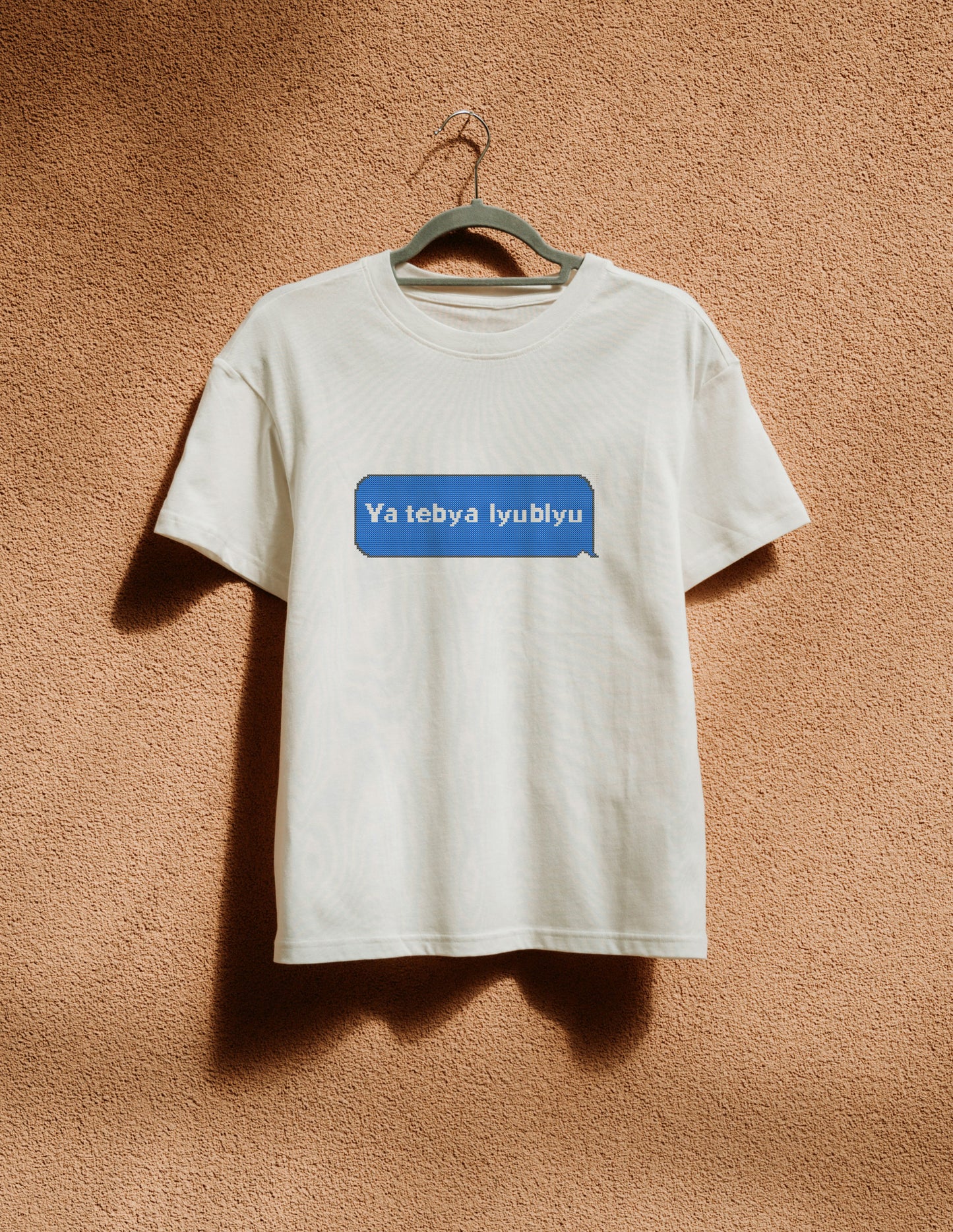 White t-shirt with a blue logo on a hanger against a brown wall