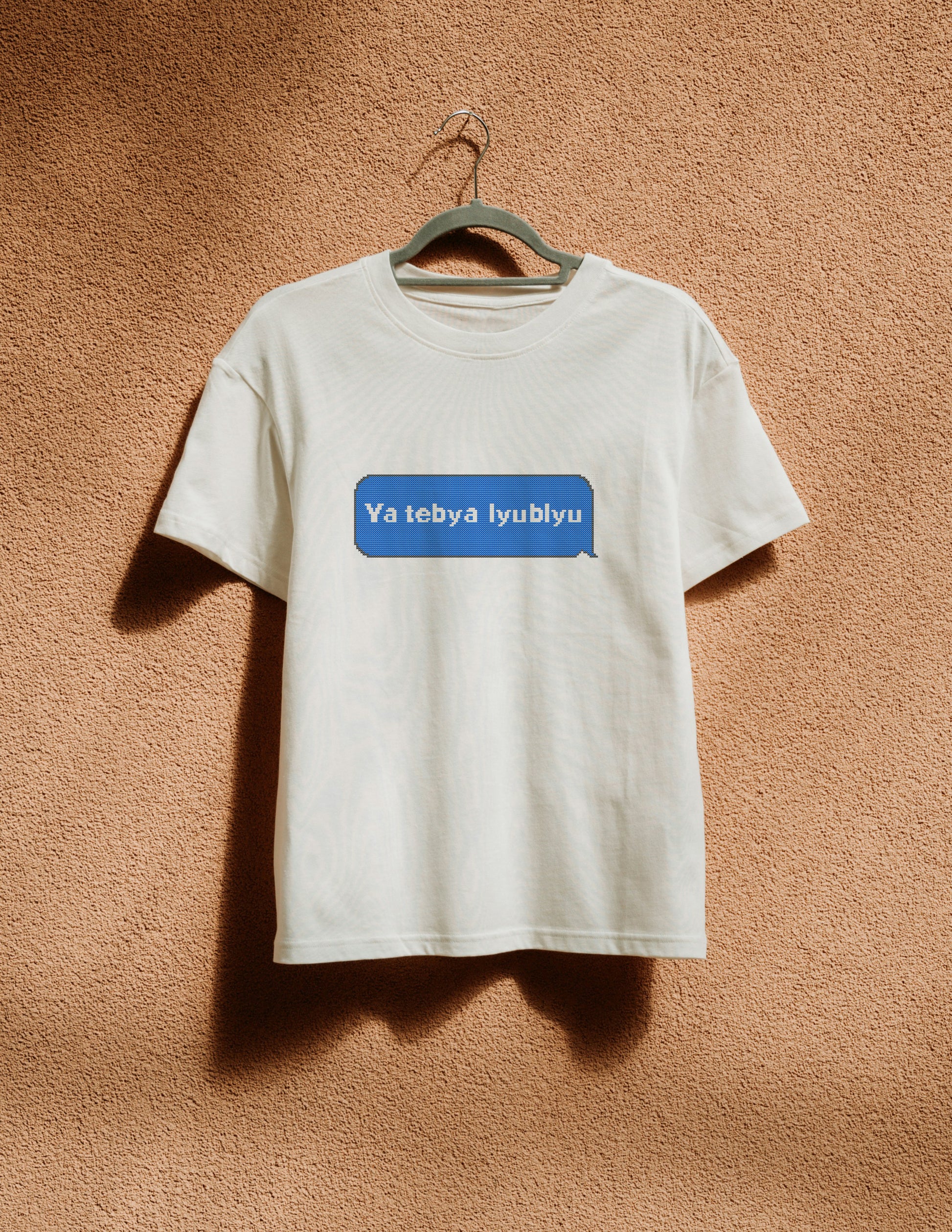 White t-shirt with a blue logo on a hanger against a brown wall