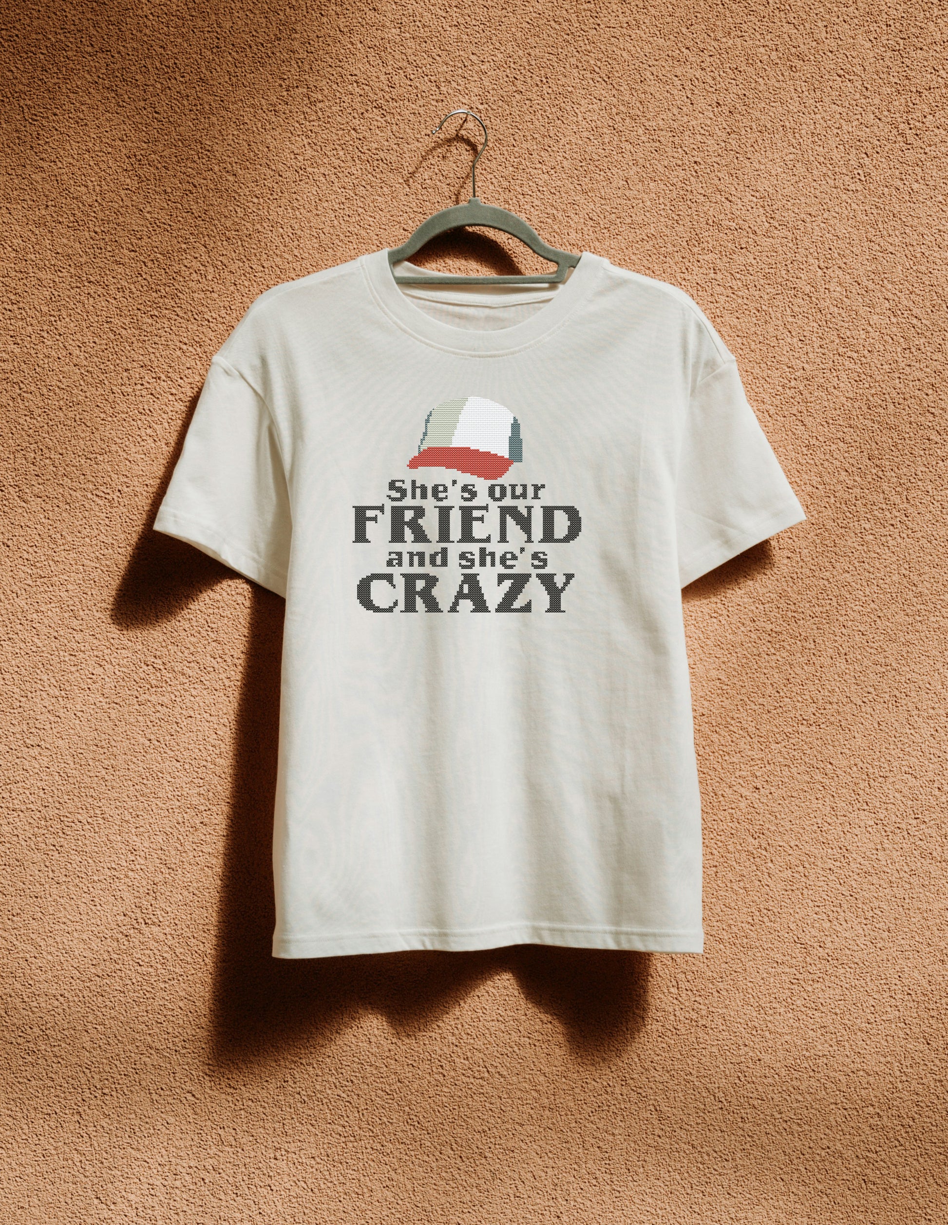 White t-shirt with graphic and text on a hanger against a brown textured wall