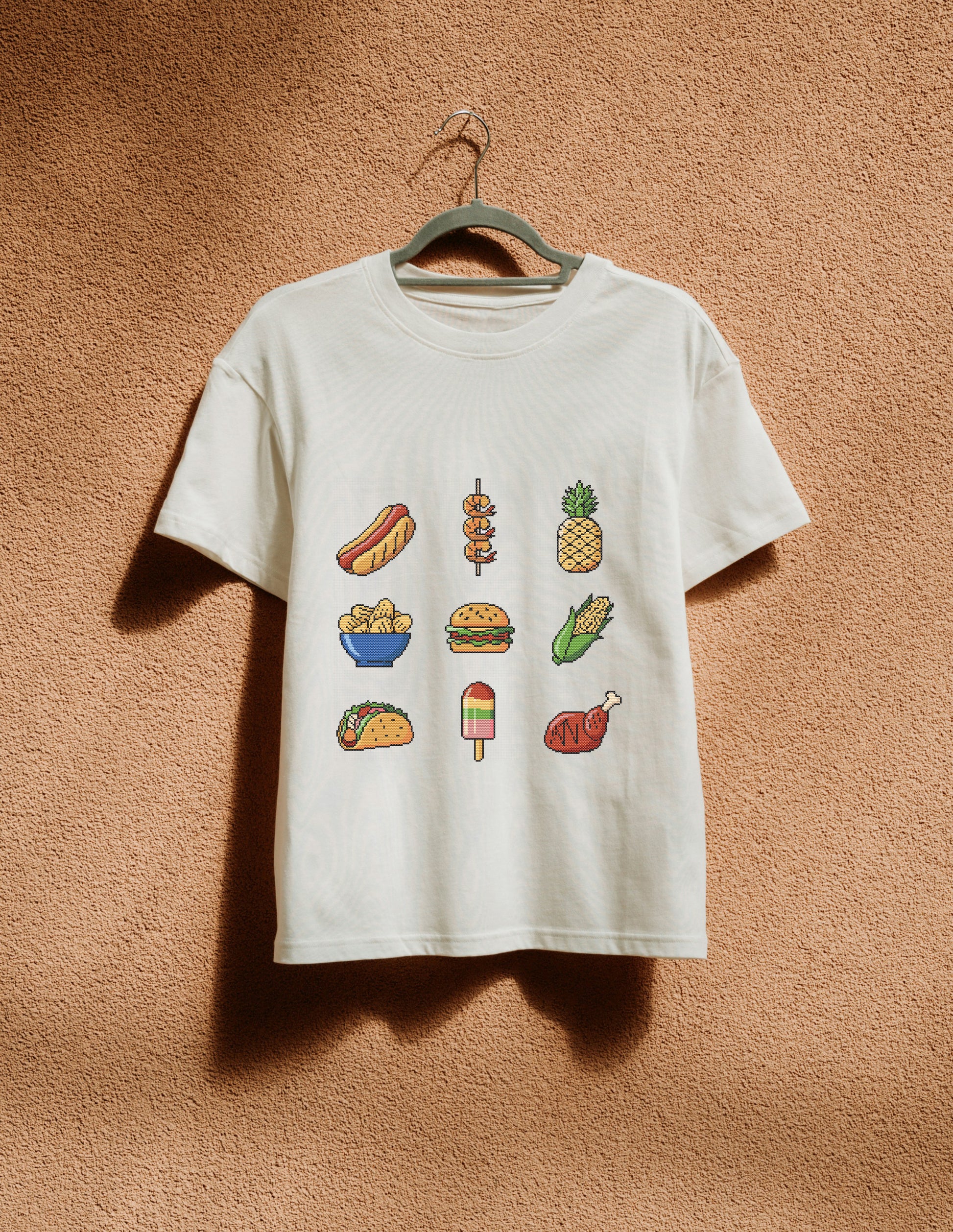 White t-shirt with food illustrations on a hanger against a brown textured wall