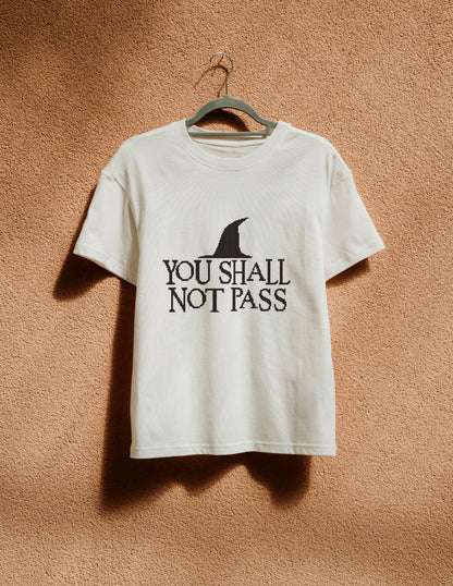 White t-shirt with 'You Shall Not Pass' text and logo on a hanger against a brown background