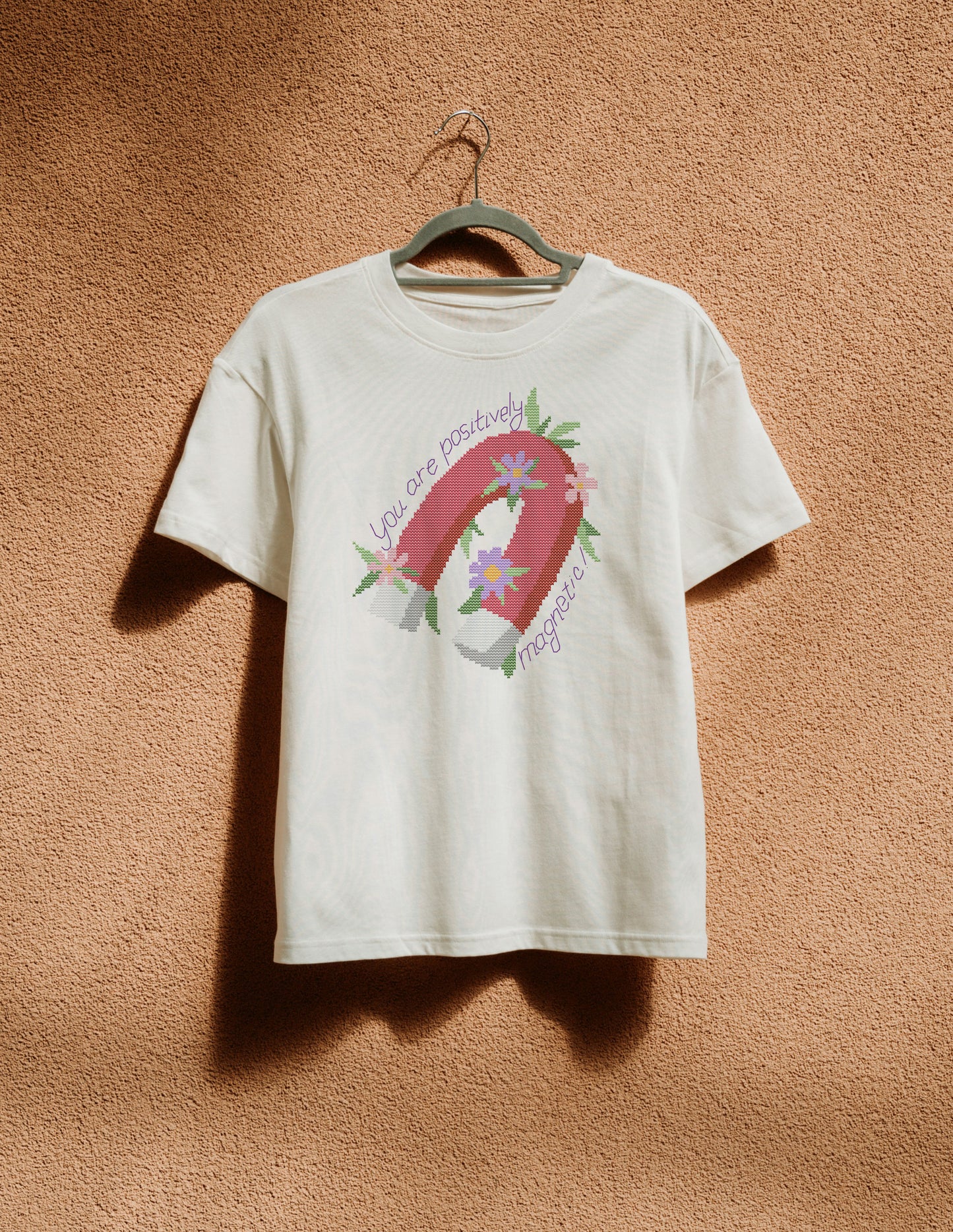 White t-shirt with a graphic design of a horseshoe and flowers on a beige wall.
