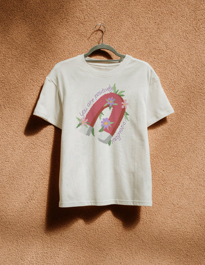 White t-shirt with a graphic design of a horseshoe and flowers on a beige wall.