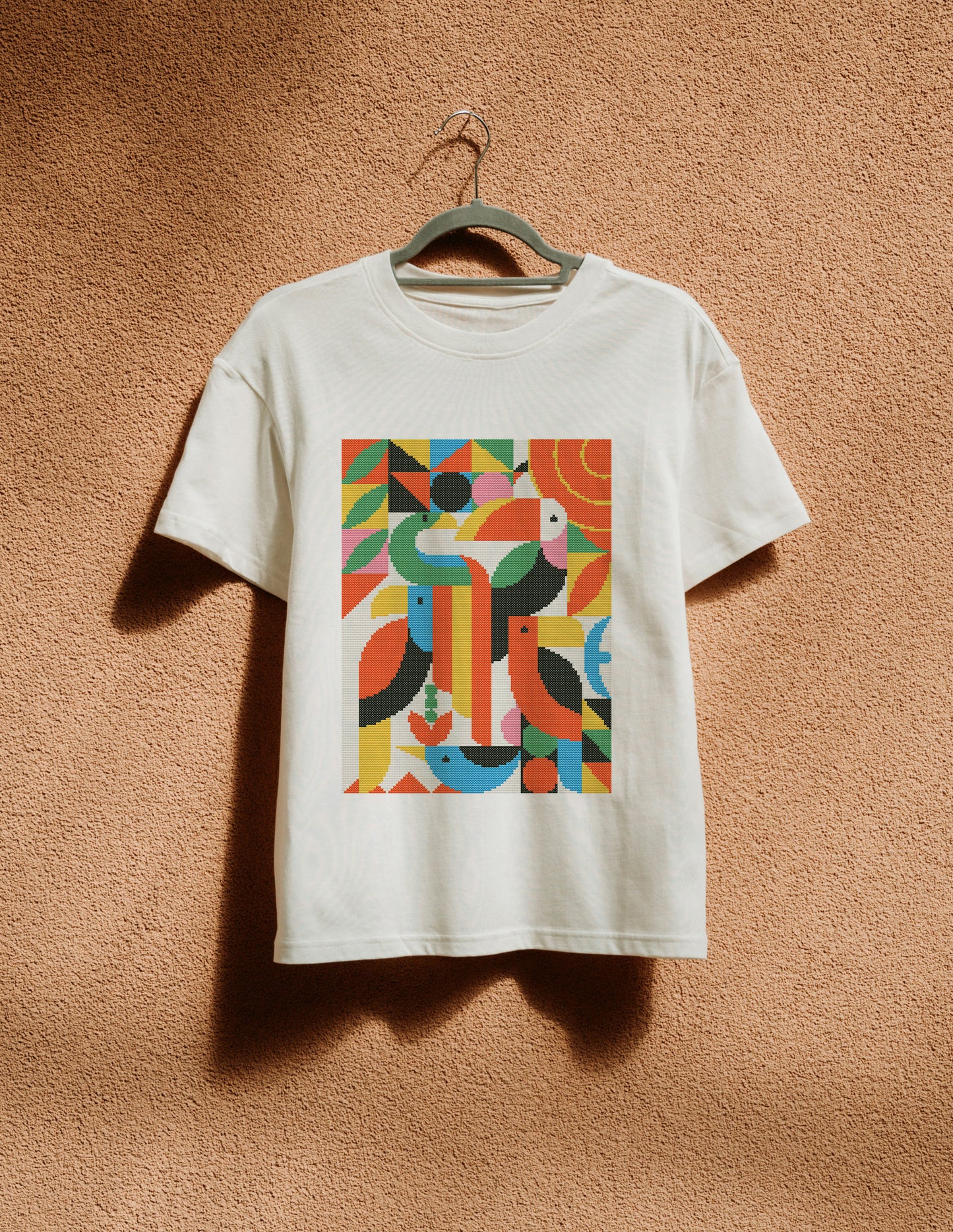 White t-shirt with a colorful geometric design on a beige wall