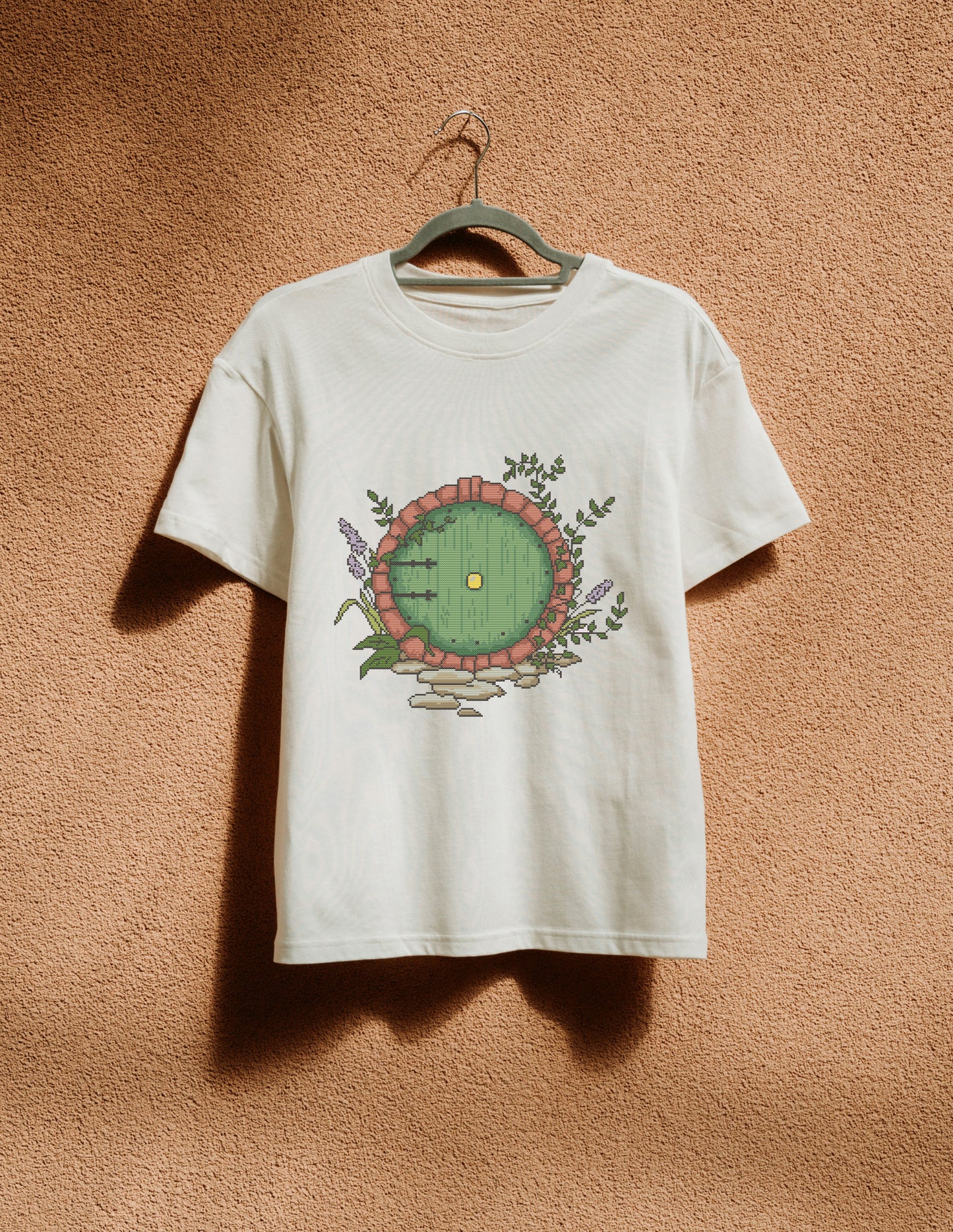 White t-shirt with a circular design hanging on a hanger against a textured brown wall.