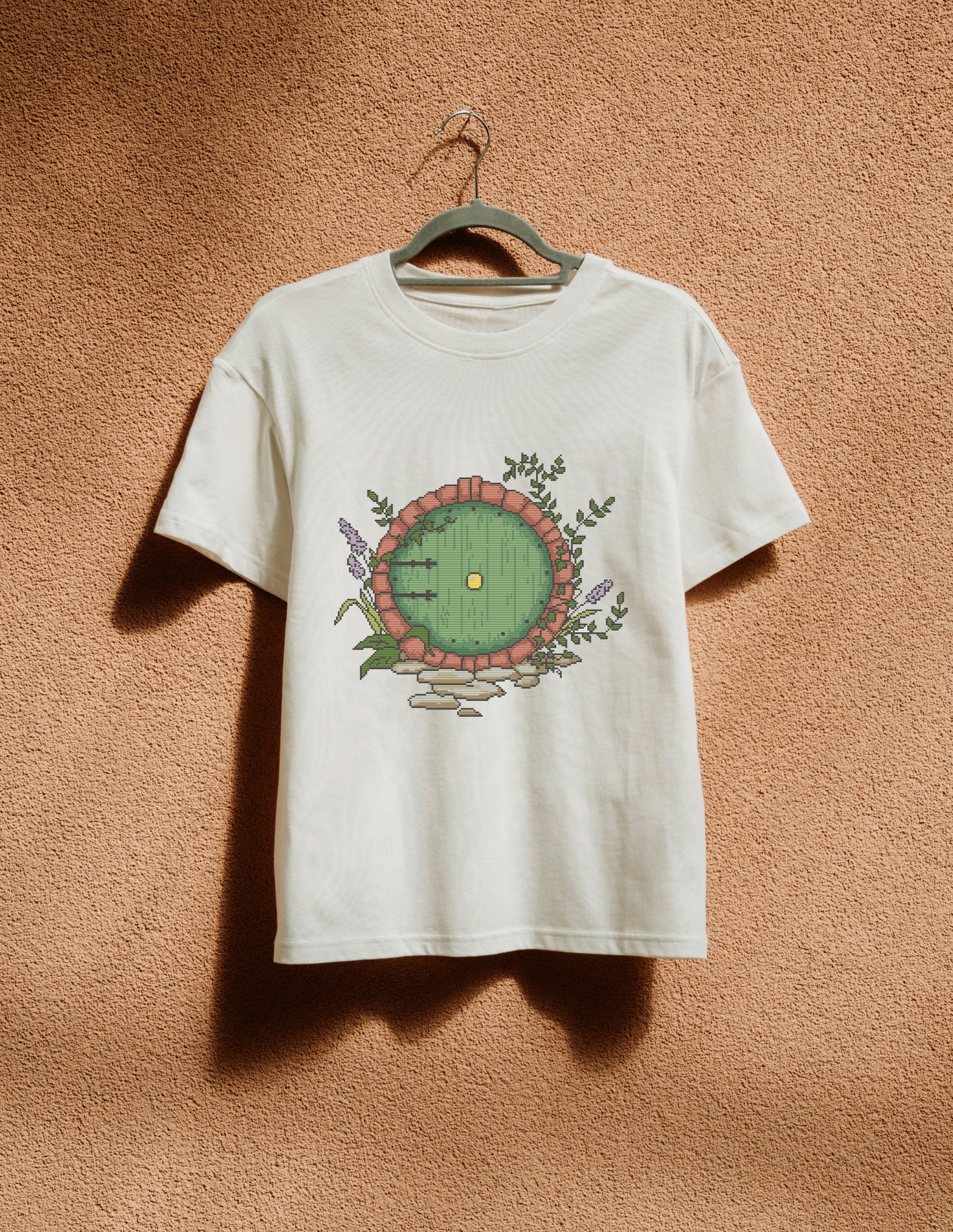 White t-shirt with a circular design hanging on a hanger against a textured brown wall.
