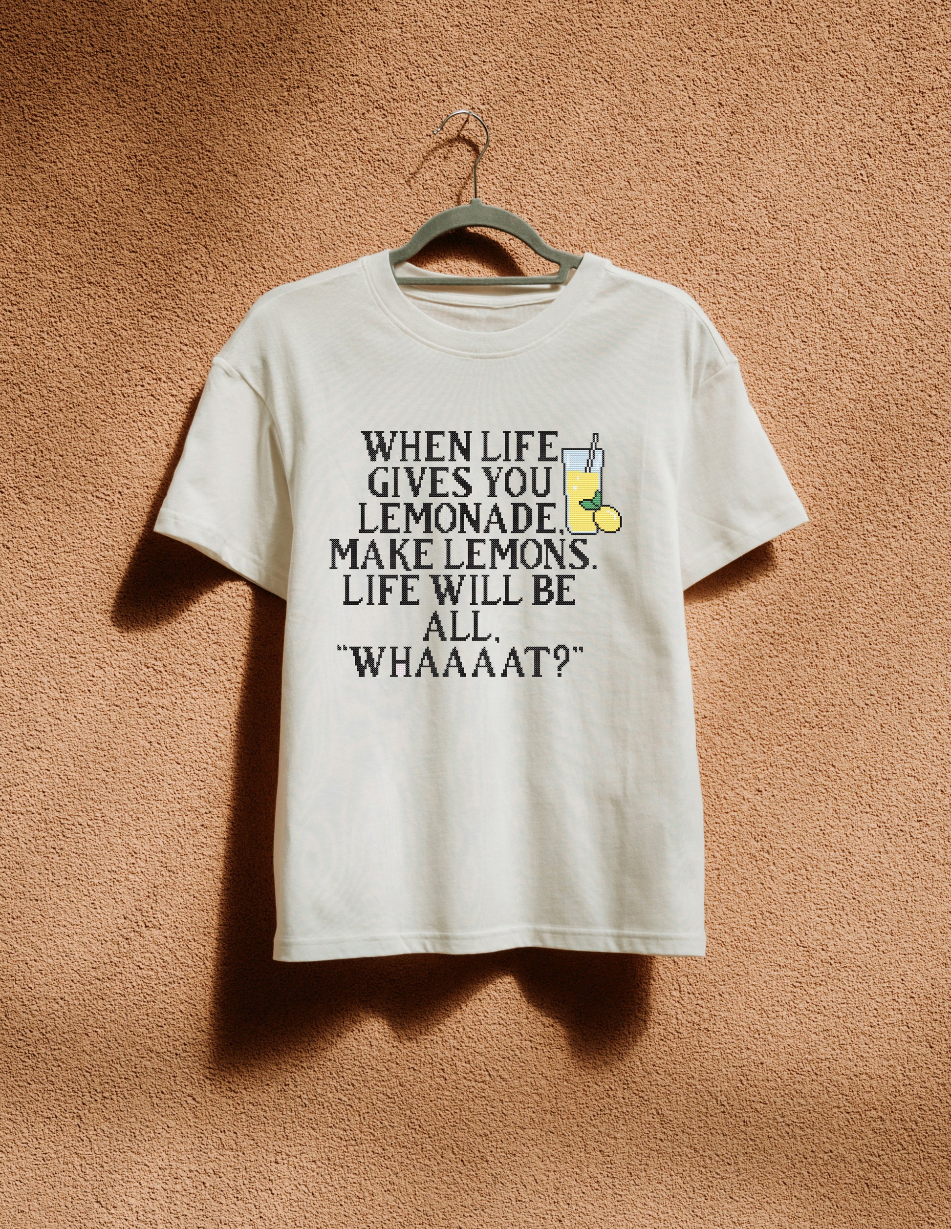 White t-shirt with humorous text design on a hanger against a textured brown wall.